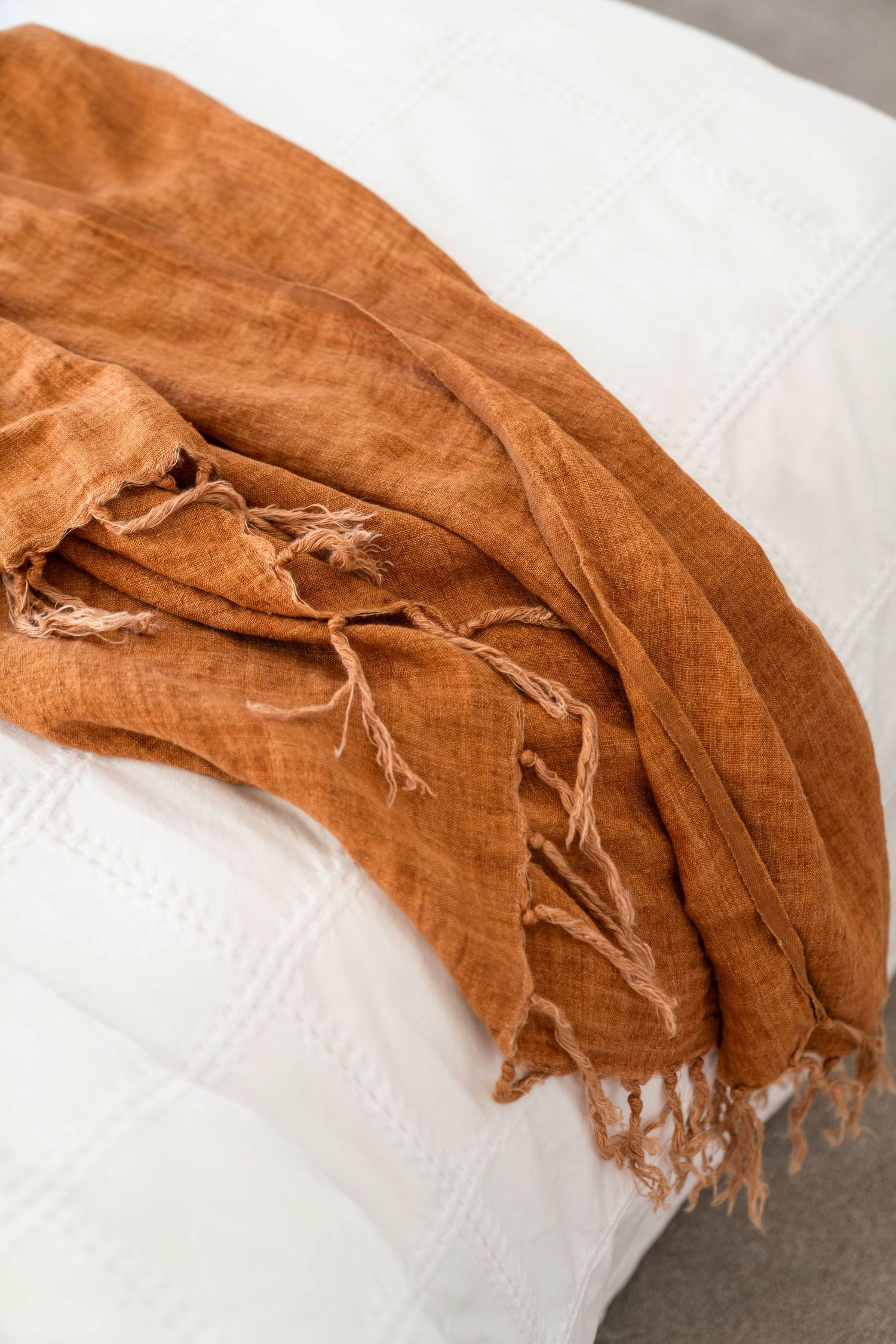 Rust-colored linen throw blanket with fringe detail draped over white surface.