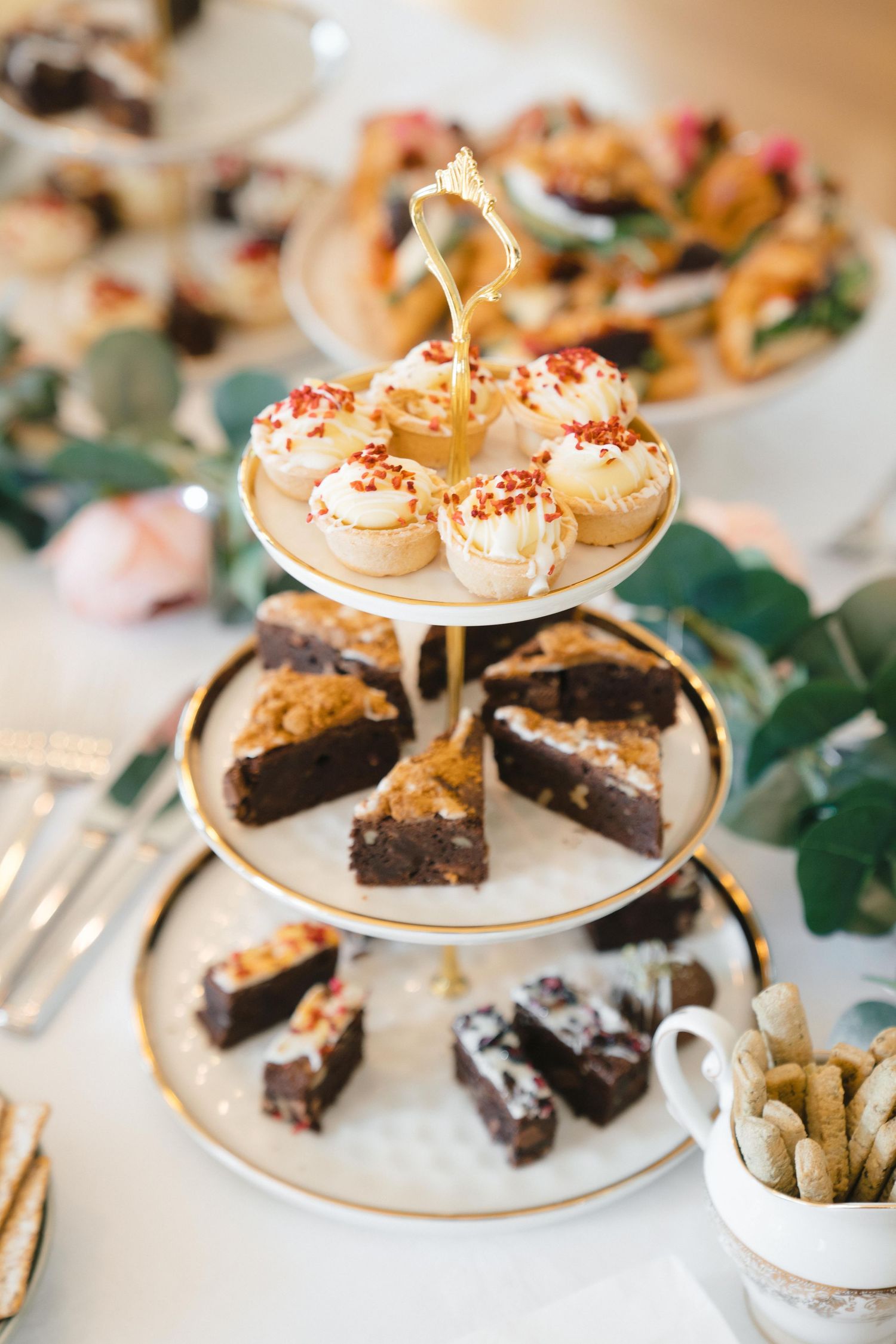 Three-tiered dessert stand with chocolate brownies and cream-topped cupcakes decorated with red sprinkles.