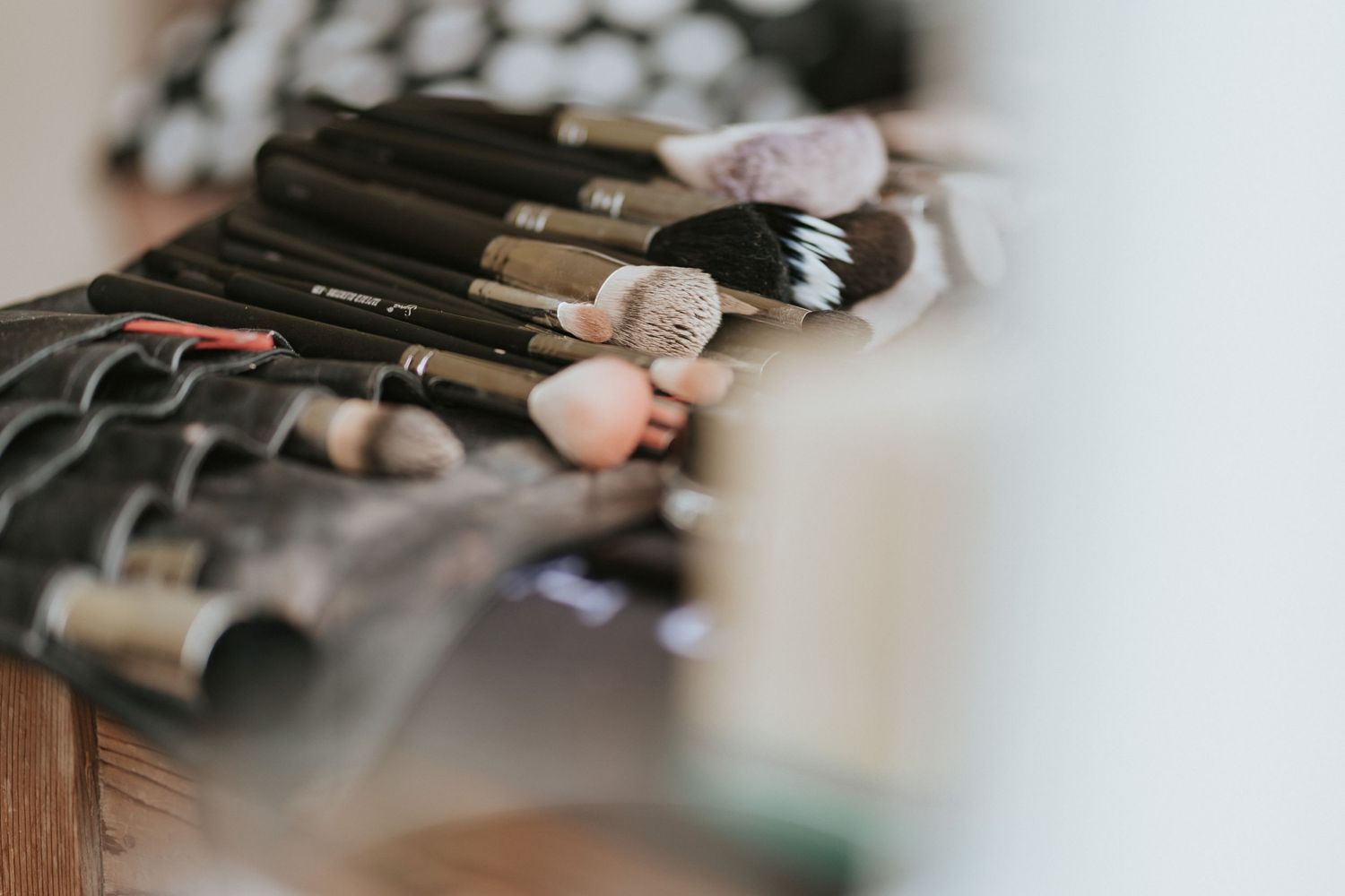 Professional makeup brushes with black handles arranged in a row on a wooden surface create a shallow depth of field.