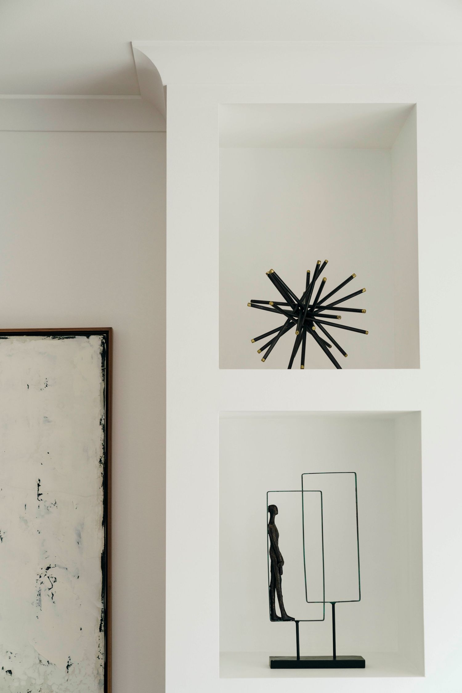 Minimalist white interior wall with black abstract art sculptures displayed in geometric niches.