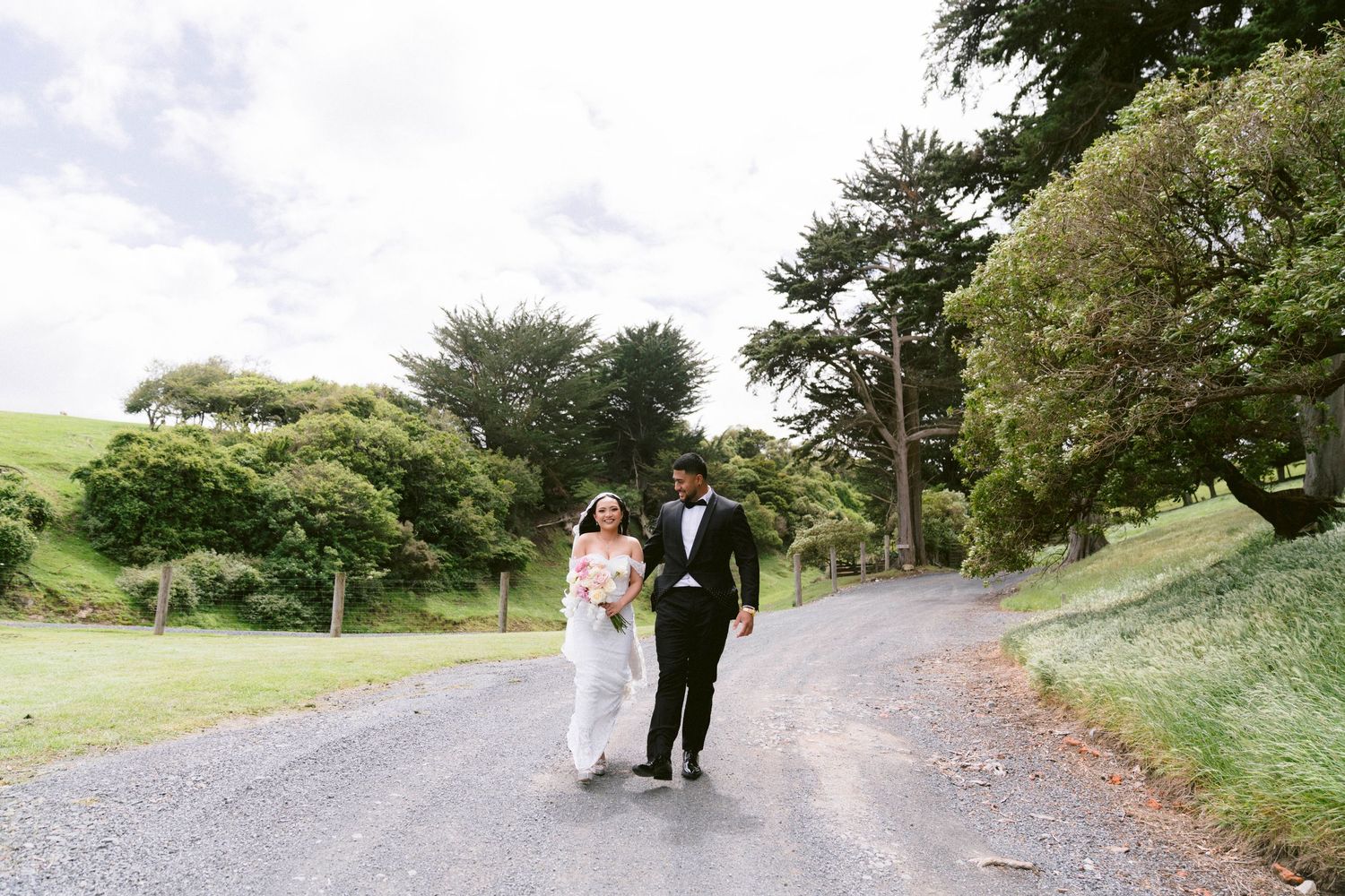 Wedding party walking along scenic outdoor path surrounded by greenery.