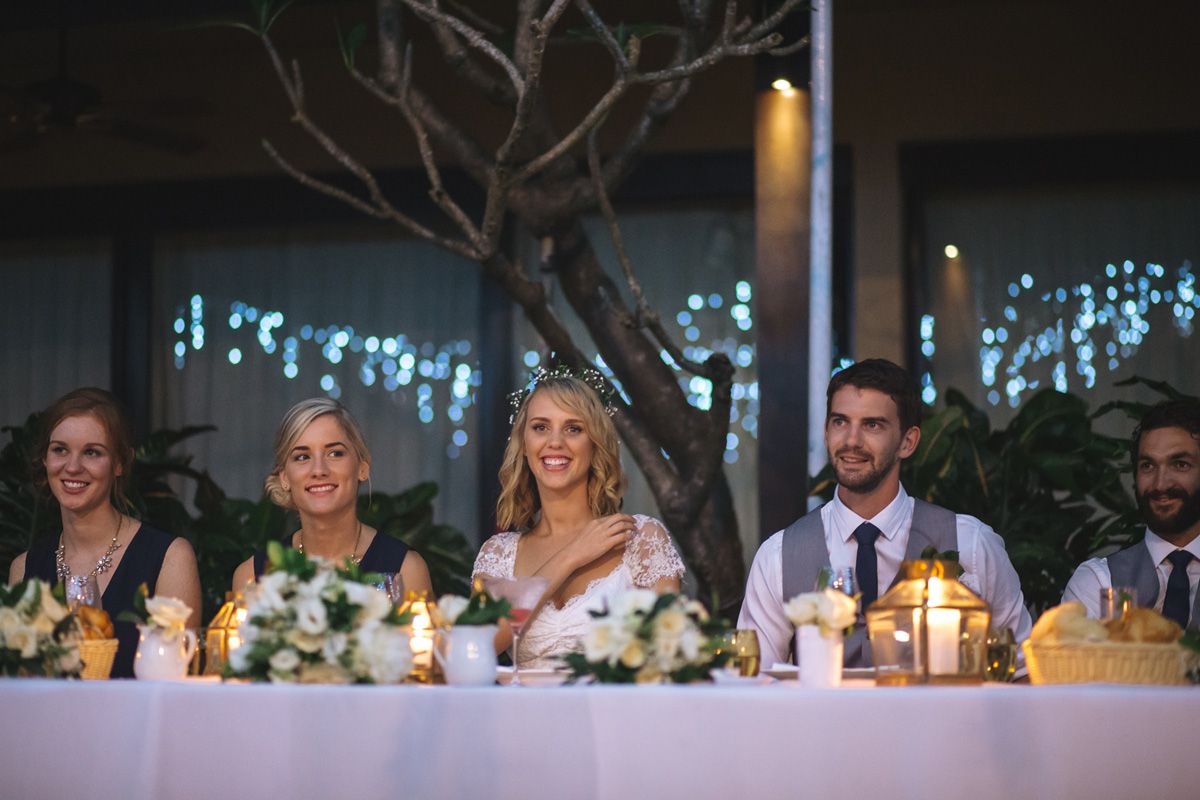Wedding reception table features glowing candles and floral arrangements with twinkling lights in background.
