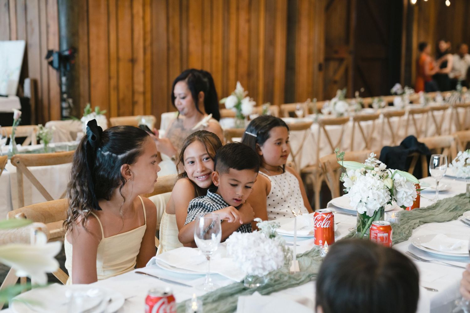Wedding reception guests enjoying a meal at long tables decorated with white linens and floral centerpieces.