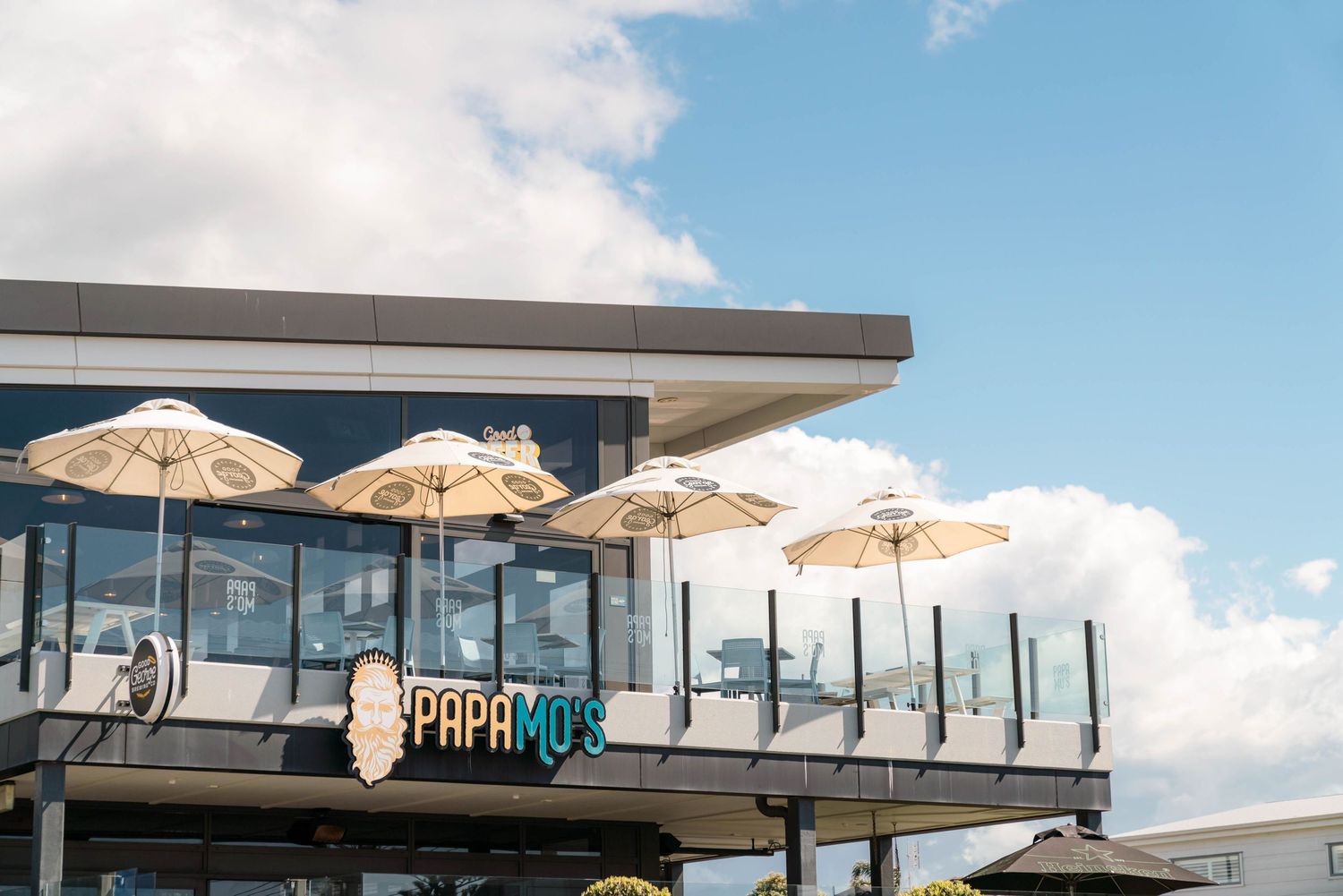 Outdoor deck with white umbrellas and glass balustrade overlooking scenic view.