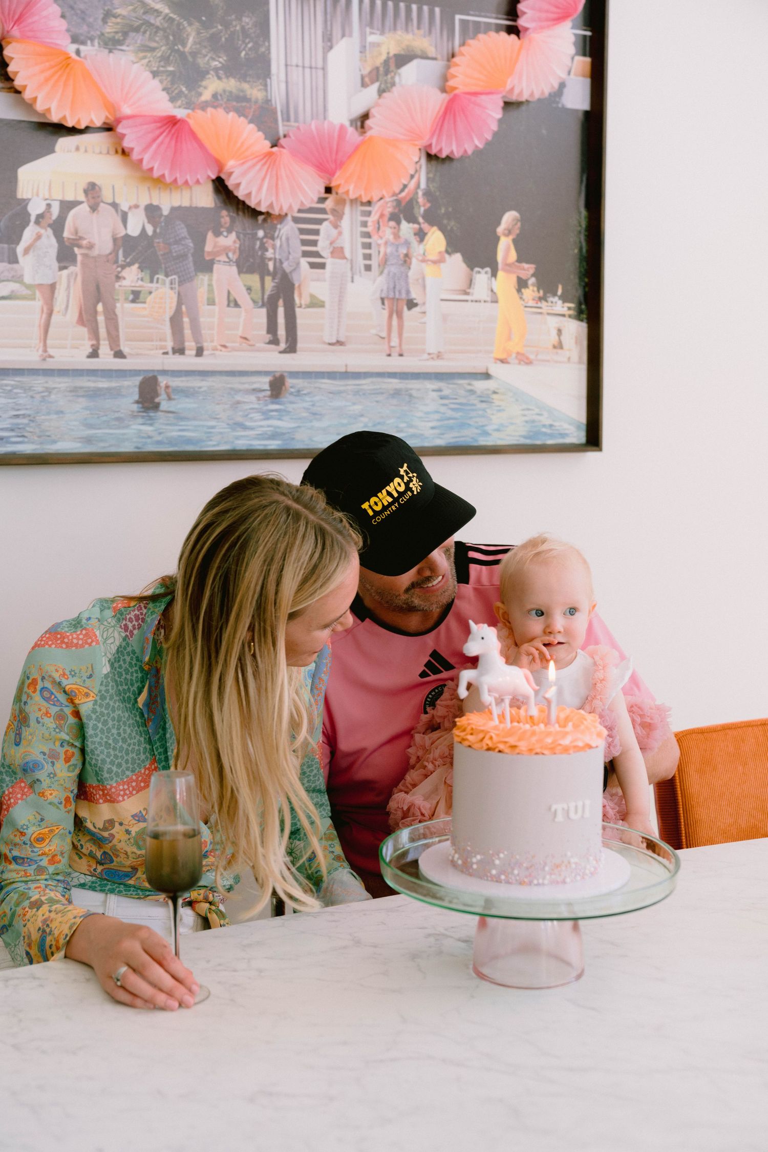 A small birthday celebration around a pink cake on a marble countertop with festive decorations.