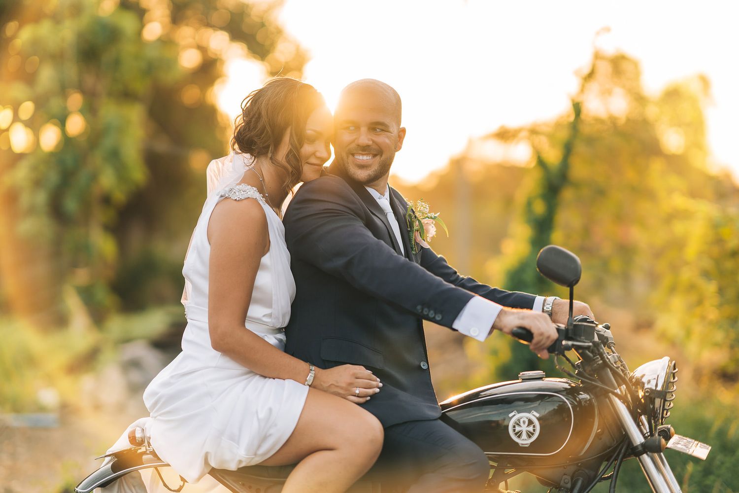 Newlyweds sharing a joyful moment on a motorcycle during golden hour.