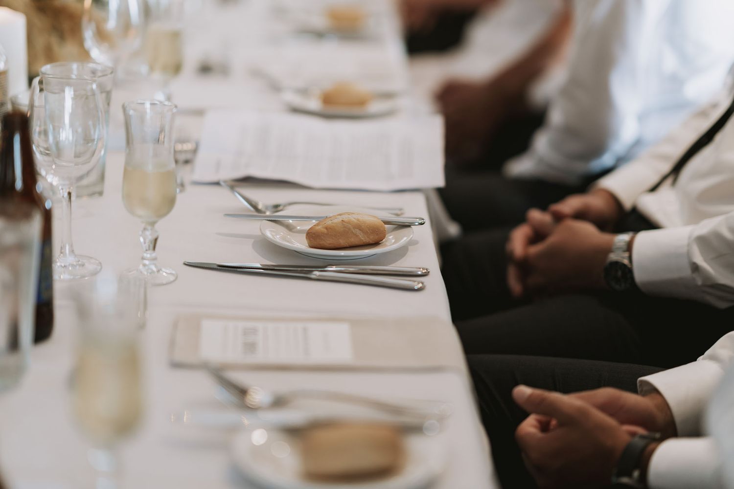 Elegant table setting at formal dinner with white tablecloth, silverware, wine glasses and guests seated.