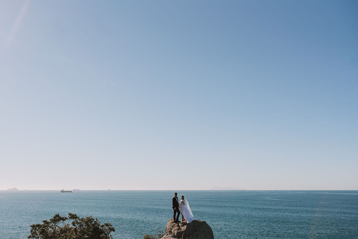 A panoramic coastal view shows a serene ocean horizon meeting a clear blue sky along a rocky shoreline.