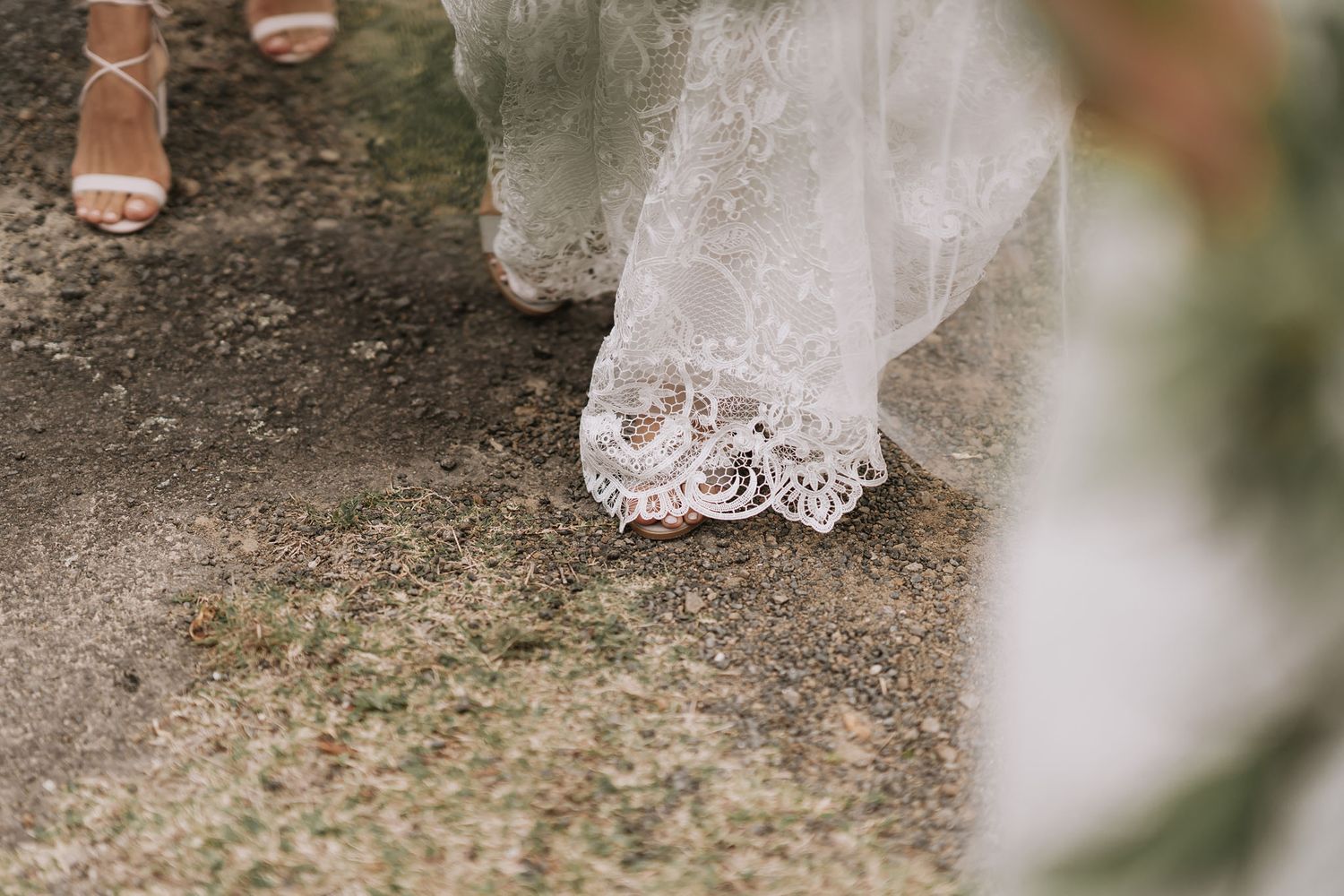 Close-up detail of delicate lace trim on a white wedding dress hem touching stone ground.