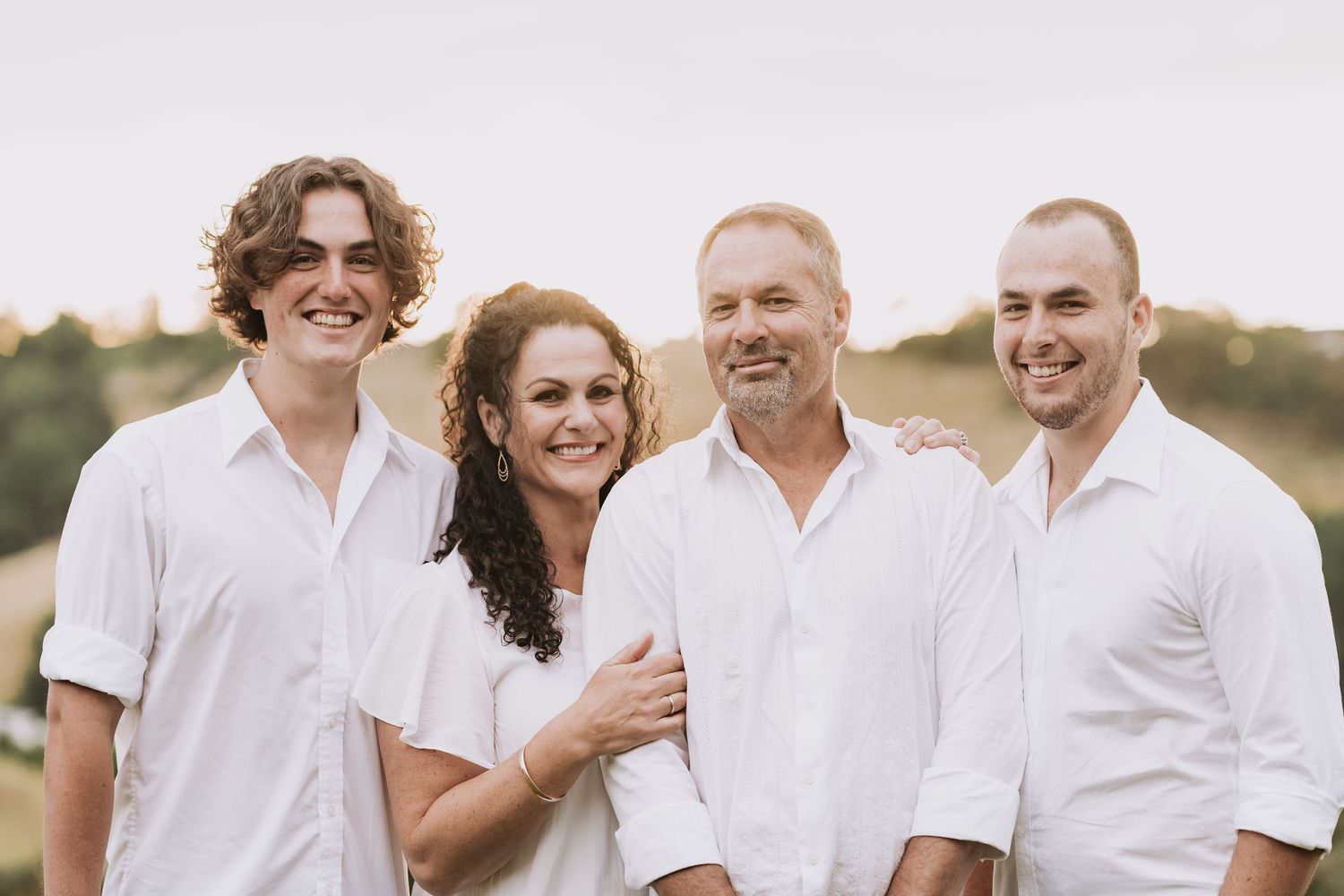 A group of four people wearing white casual shirts pose together outdoors on a sunny day.