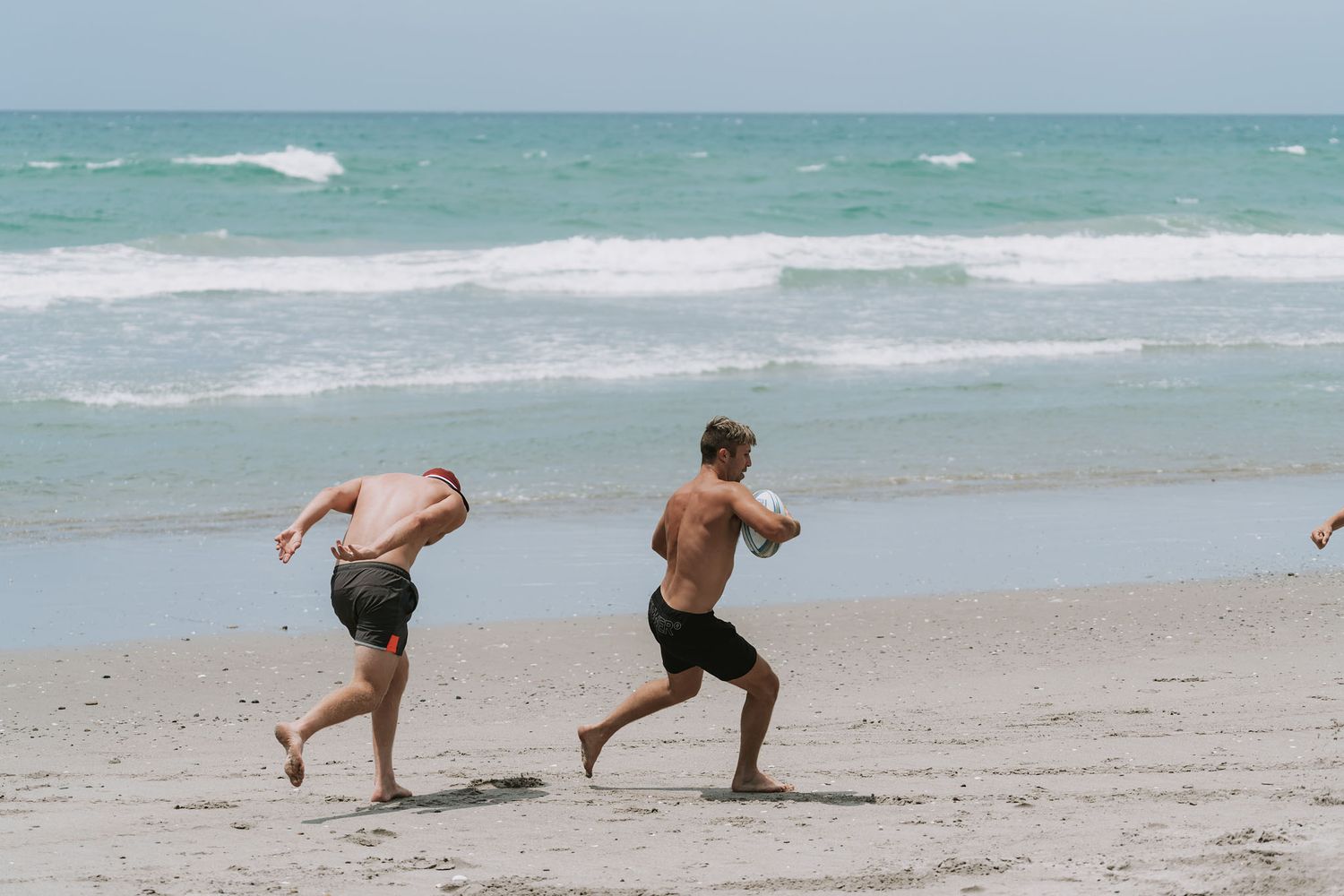 Two people practicing yoga poses together in sequence on a sandy beach with turquoise ocean waves in the background.