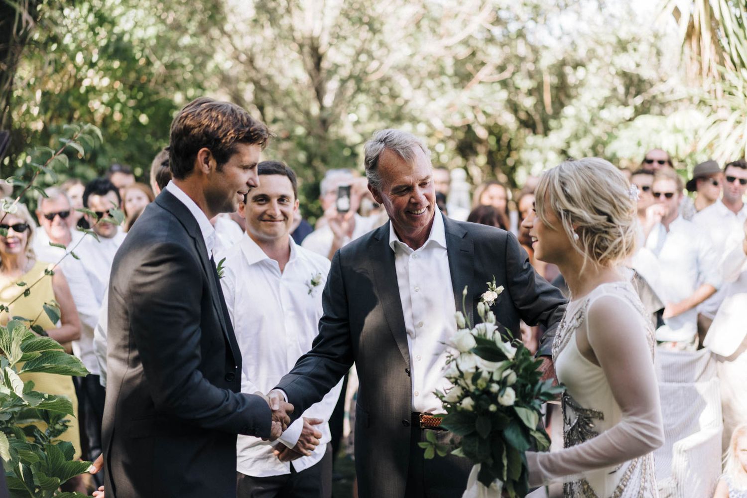 A wedding party celebrates outdoors with a series of group hugs and embraces at a joyful outdoor celebration.