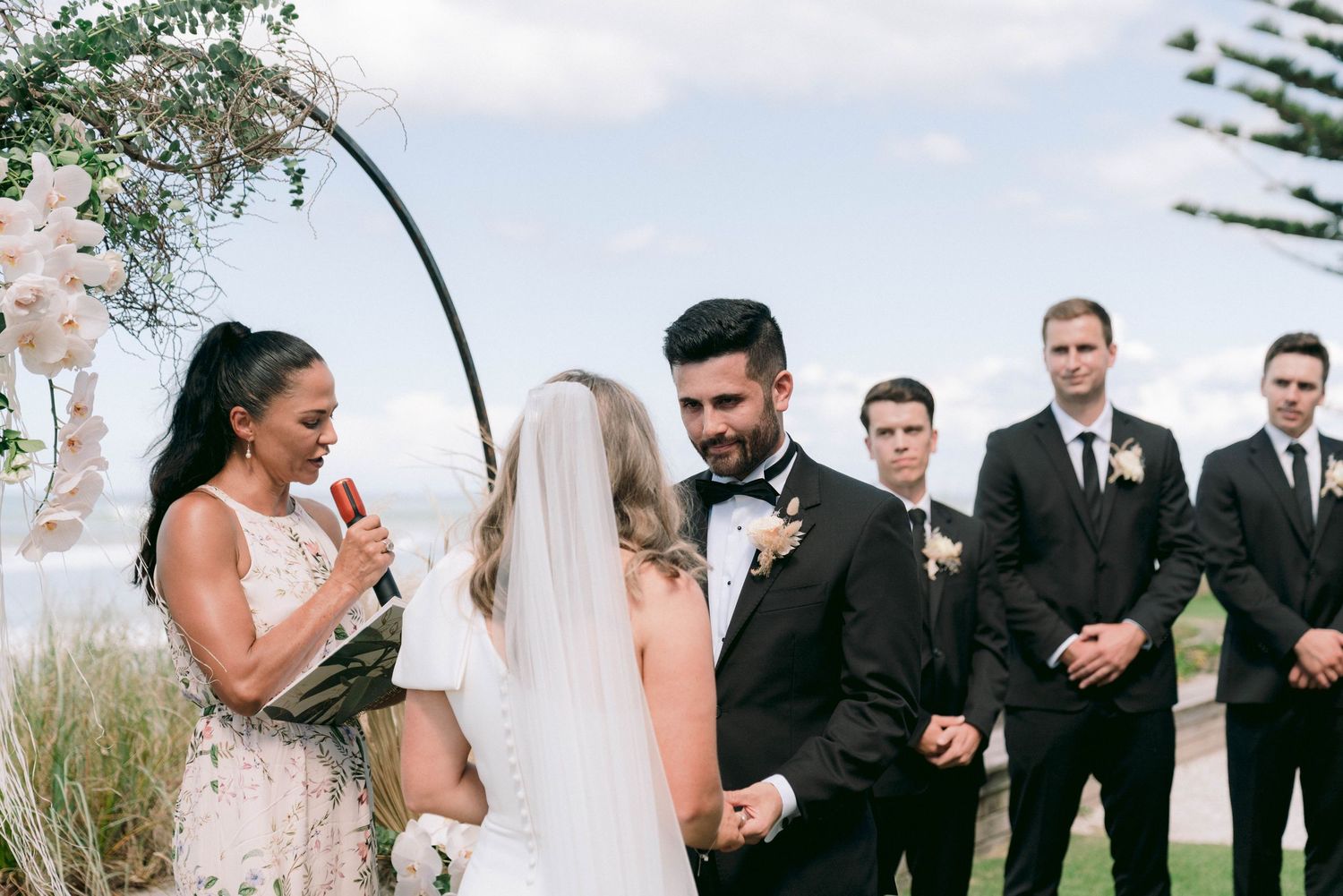 Wedding party gathered outdoors with groomsmen in black suits and bridesmaids in light dresses.