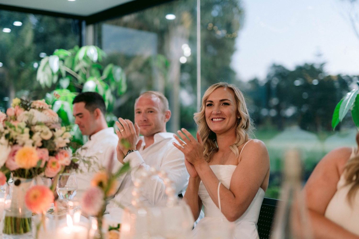 Wedding guests share emotional reactions during a reception dinner with floral centerpieces and ambient lighting.