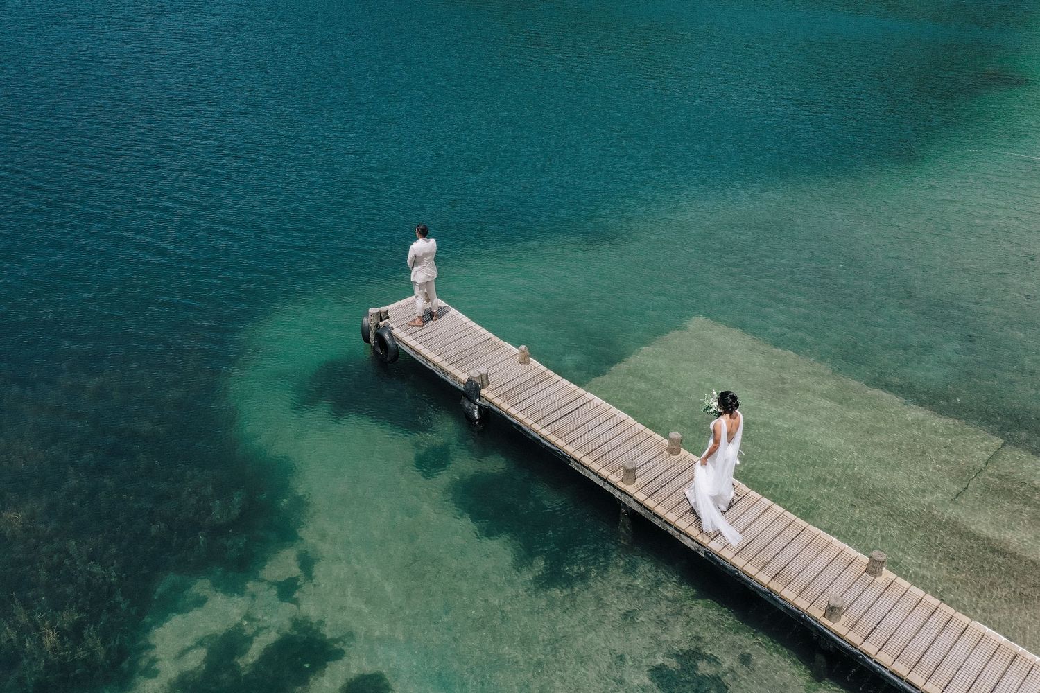 Wooden dock extending over turquoise waters with people enjoying peaceful moments.