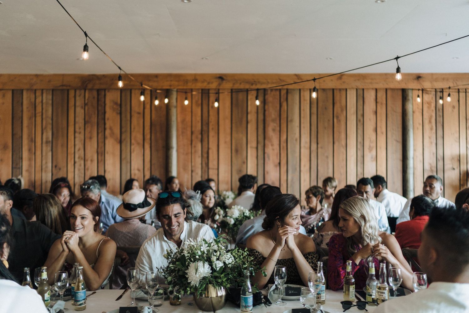 Modern wooden barn venue interior filled with guests at long tables during reception dinner.