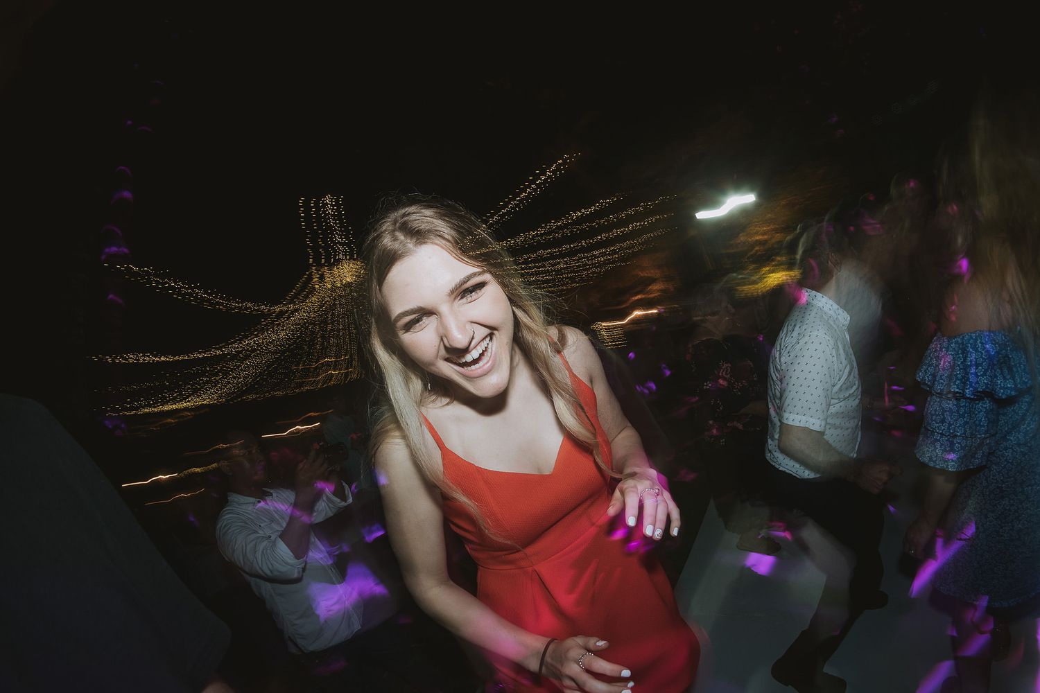 Woman dancing at a nightclub with light trails and colorful lighting effects in the background.