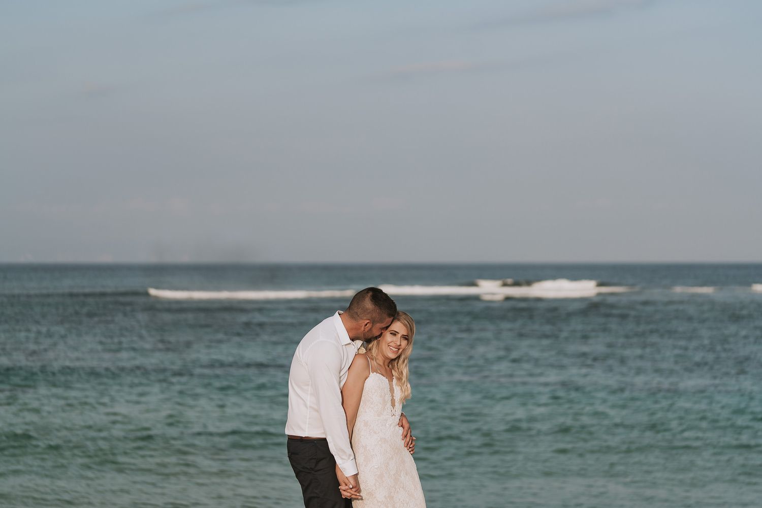 Romantic beach wedding scene with gentle waves and boats on the horizon during sunset.