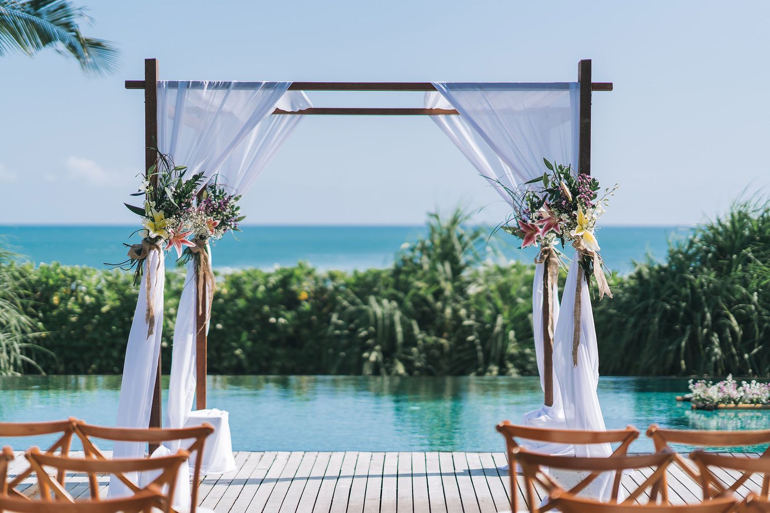 Elegant beach wedding arch with white fabric and floral decorations overlooking the ocean.