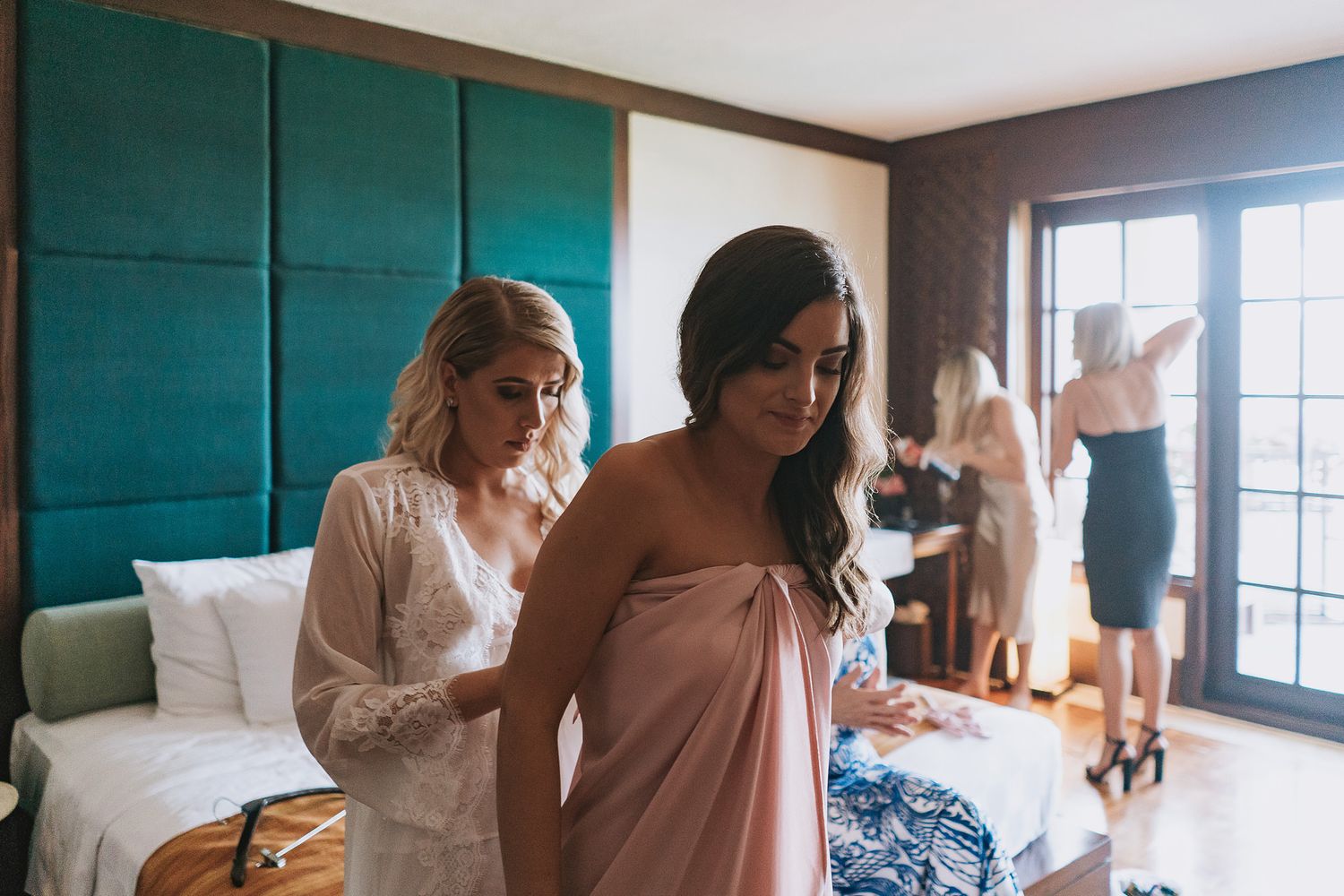 Bridesmaids helping with wedding preparations in a hotel room with teal wall panels.