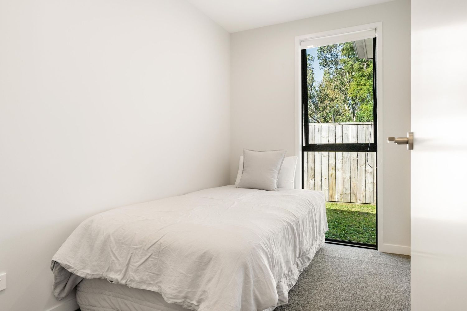 Clean white bedroom with floor-to-ceiling windows providing natural light and garden views.