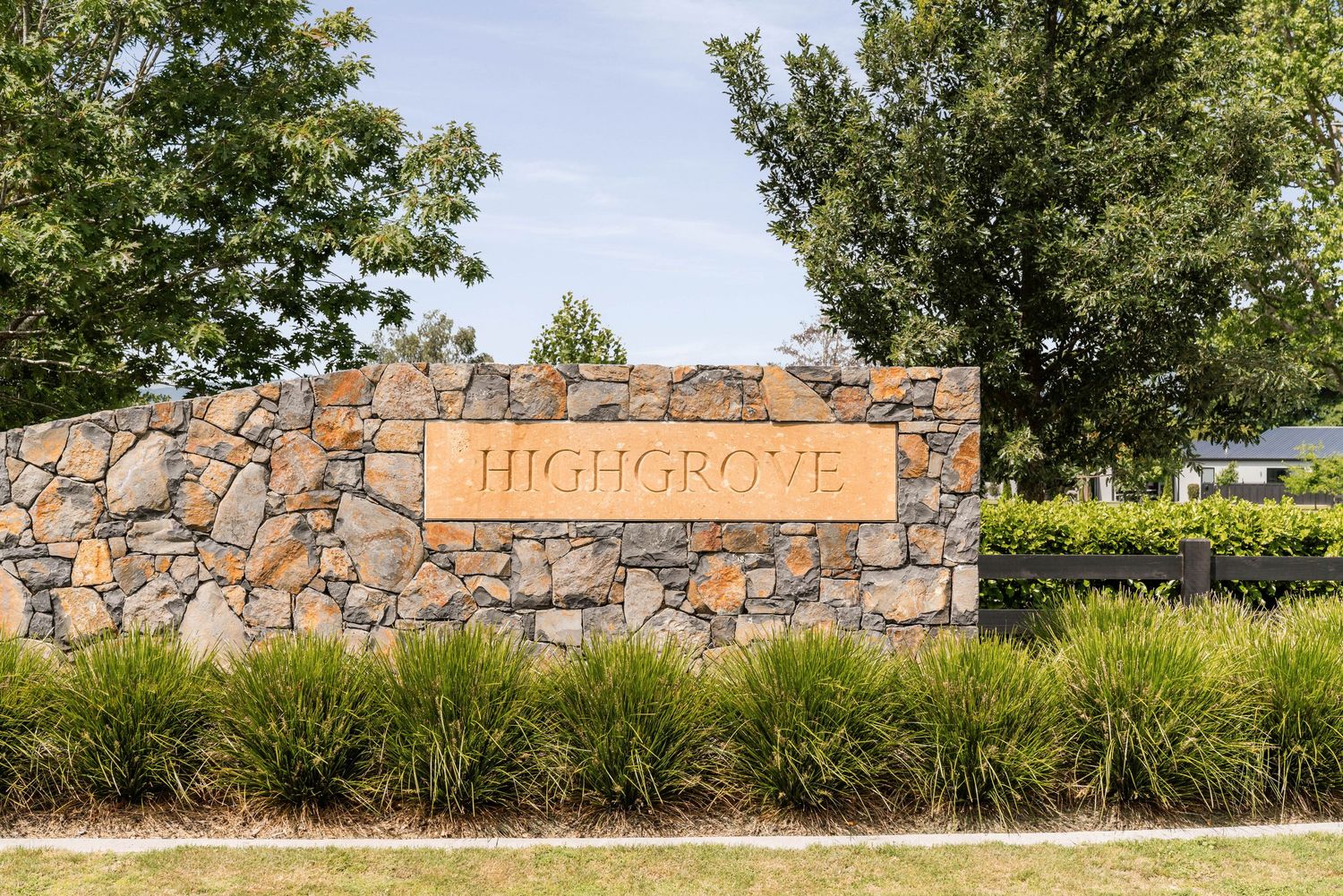 Stone wall entrance sign reading 'Highgrove' with ornamental grasses and trees.