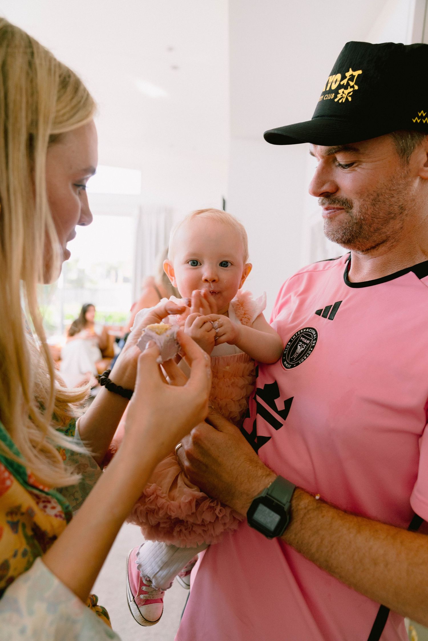 A small baby in a pink tutu outfit being held while others gather around.
