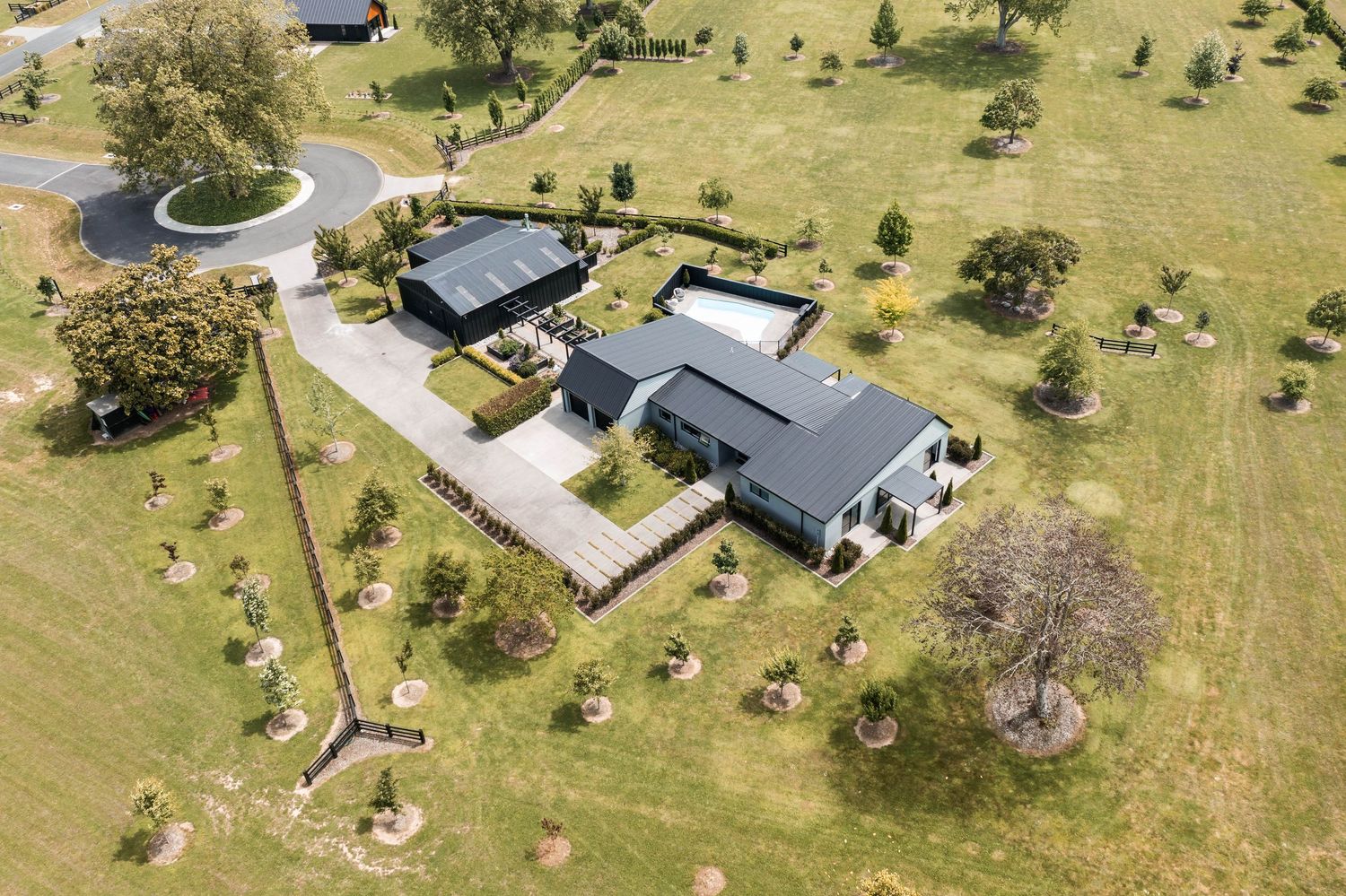 Aerial view of a rural property with multiple buildings and large grassy areas surrounded by scattered trees.