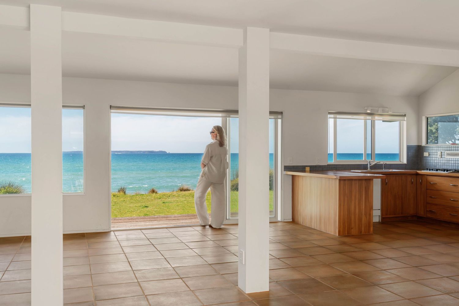 Open concept beach house interior with white posts, tiled floors and panoramic ocean views through large windows.