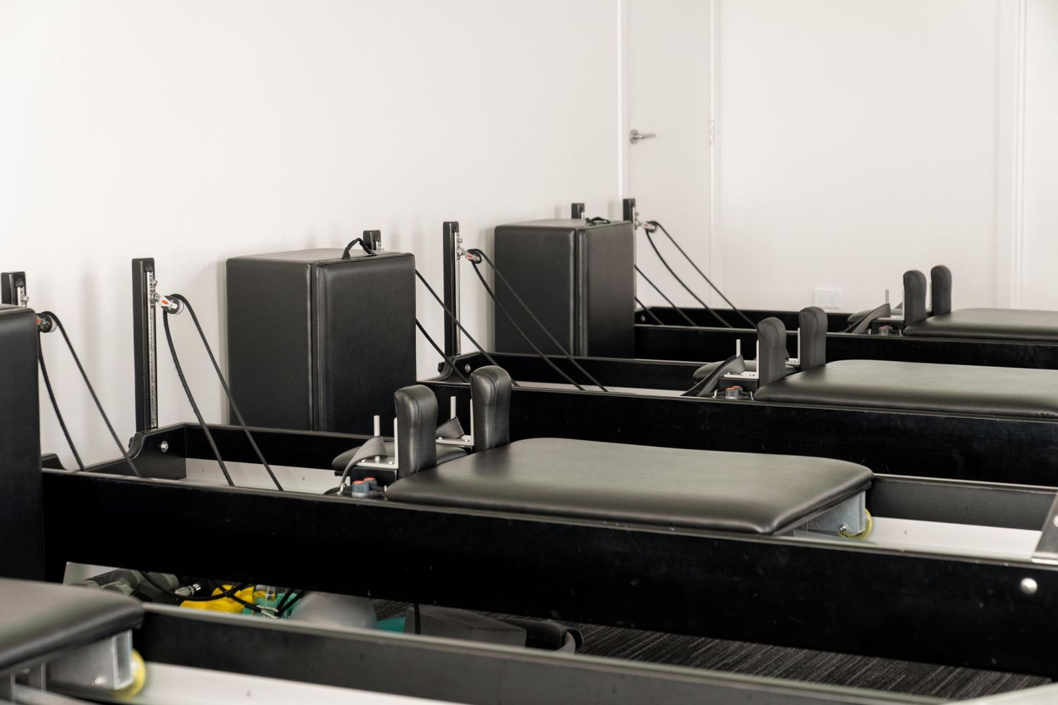 Row of black Pilates reformer machines in a fitness studio.