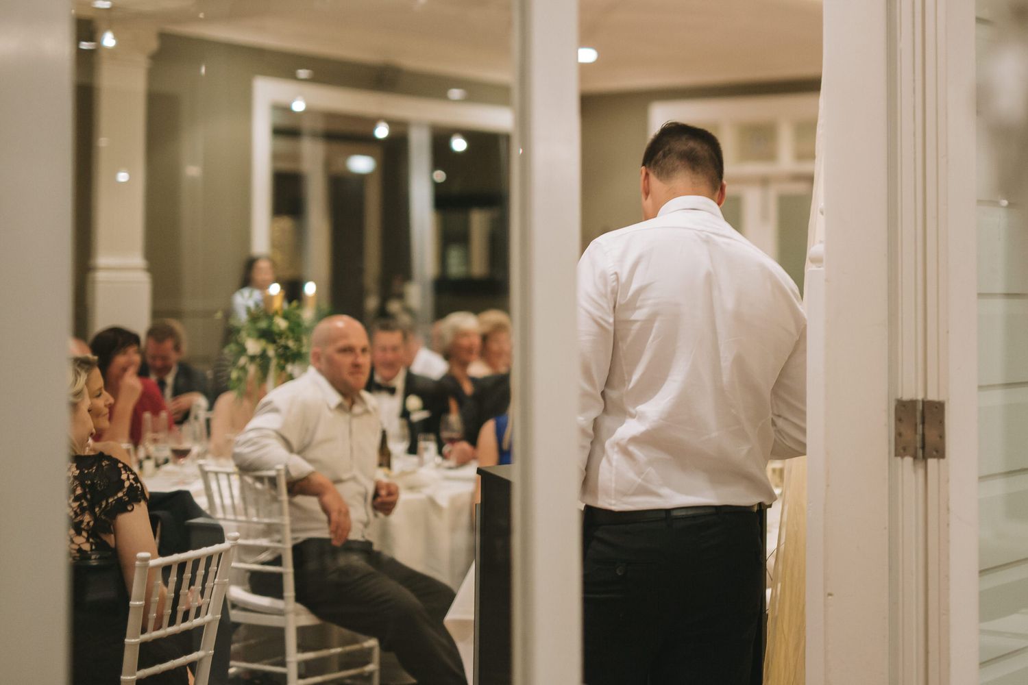 A person in white dress shirt standing in a doorway during a wedding reception event.