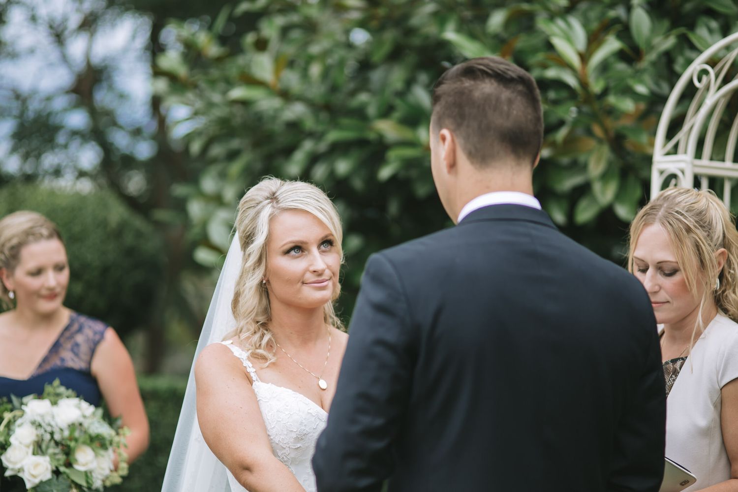 A couple exchanging vows during an outdoor garden wedding ceremony with bridesmaids looking on.