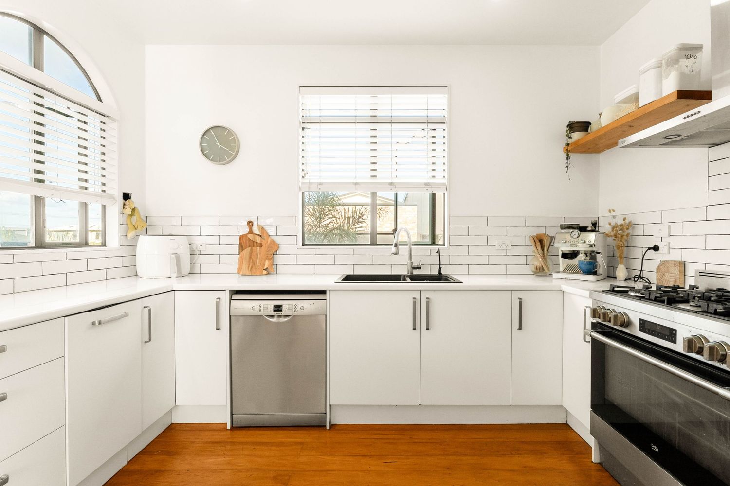 Modern white kitchen with subway tile backsplash, wood floors, and stainless steel appliances.