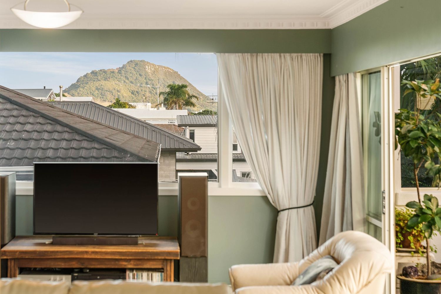 Modern living room with green walls, white curtains and mountain views through large windows.