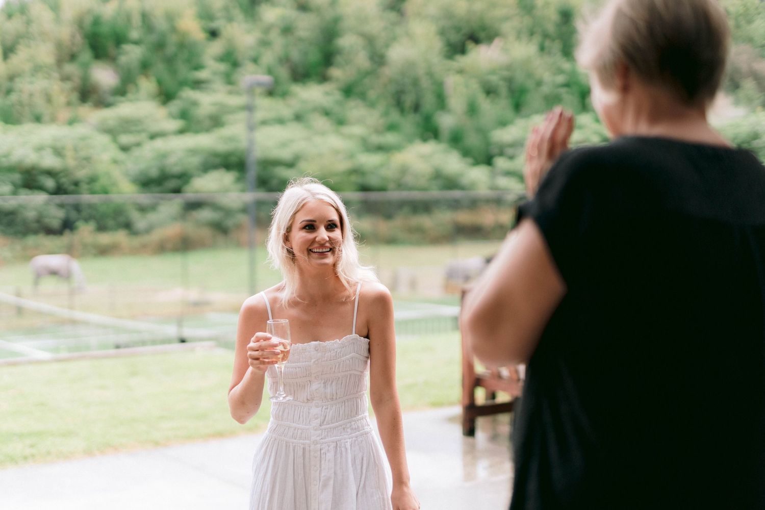 A bride in a white lace dress reacts emotionally during a wedding celebration outdoors.
