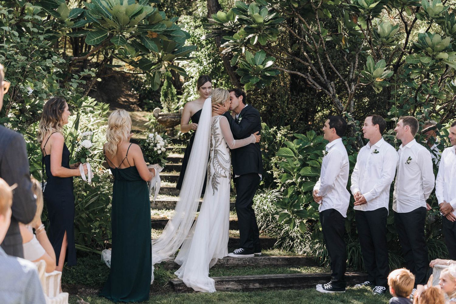 An outdoor wedding ceremony in a garden setting surrounded by lush greenery and trees.
