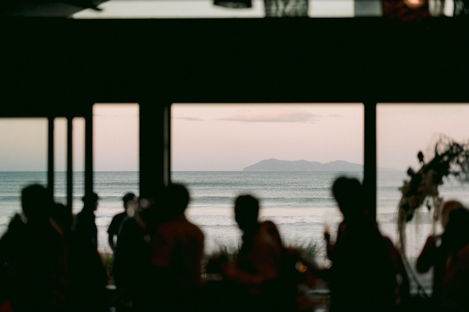 Silhouetted guests enjoying sunset reception with ocean view.