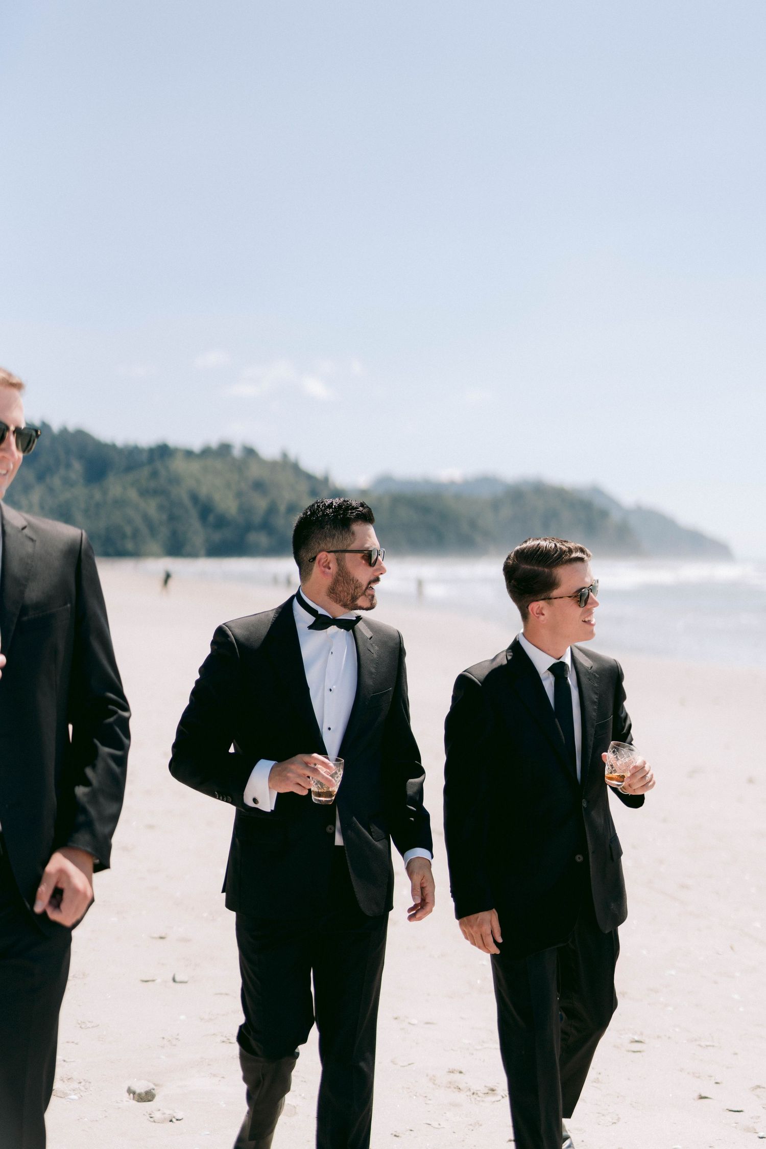 Well-dressed guests in formal attire walking along a scenic beach on a sunny day.