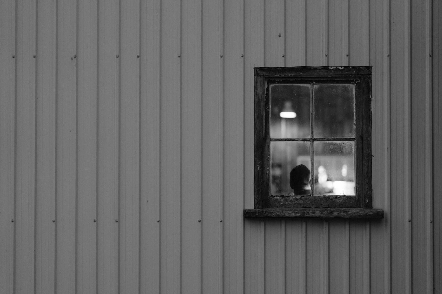 Row of black and white photographs displayed on a wall next to small illuminated window showing architectural details.