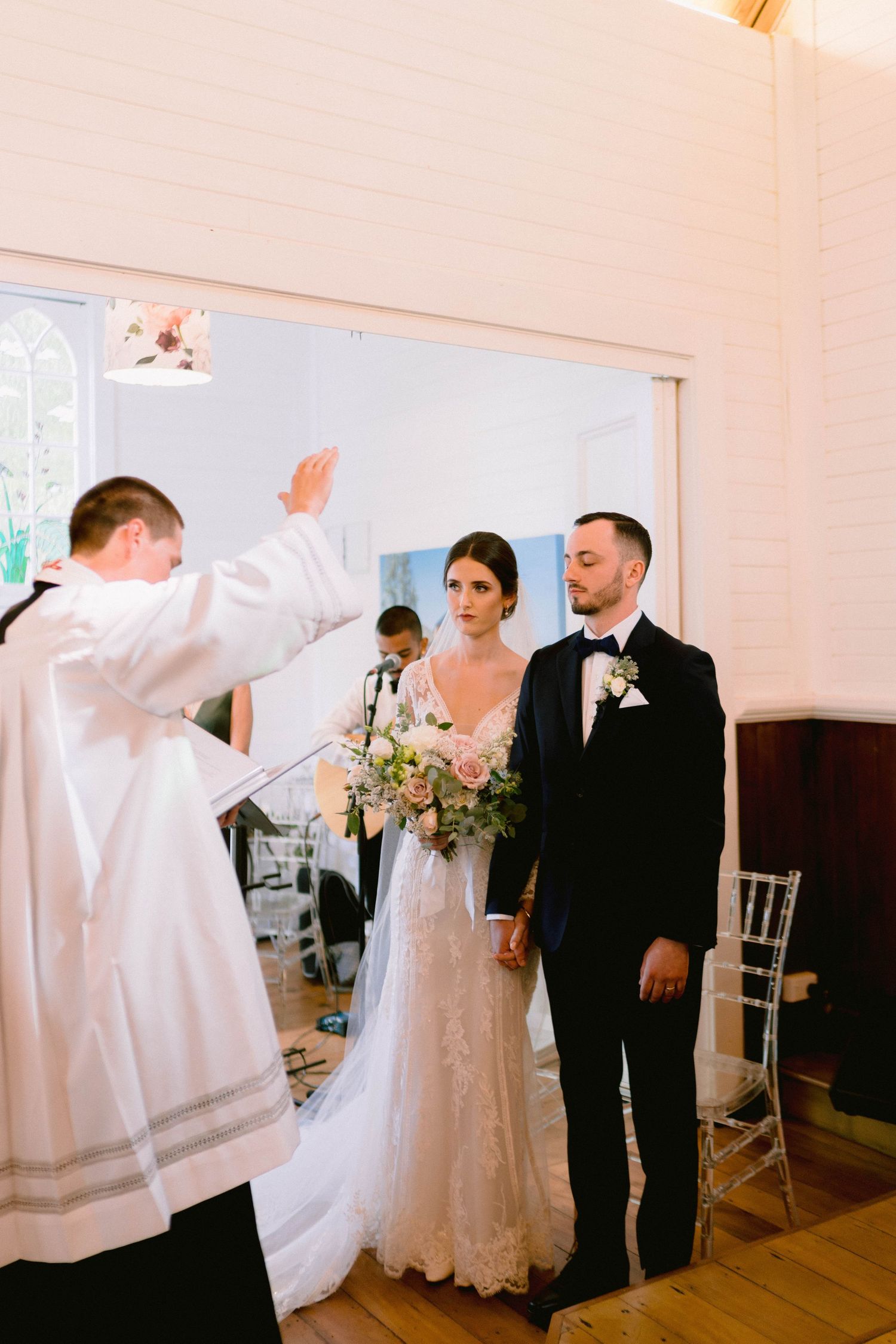 Wedding ceremony moment with priest blessing the couple in a chapel.
