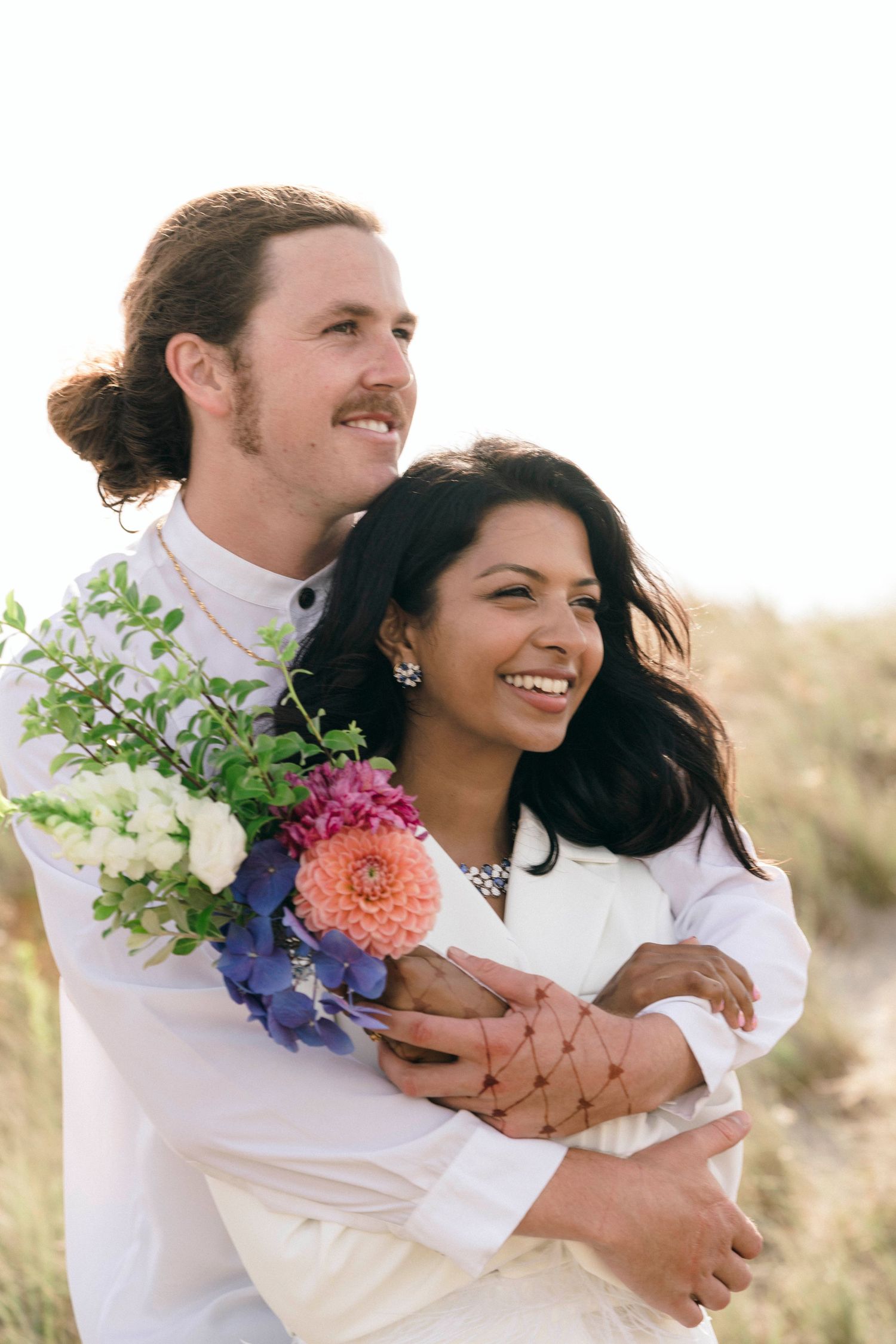 Close-up of couple sharing an intimate embrace while holding a colorful wedding bouquet on a beach.