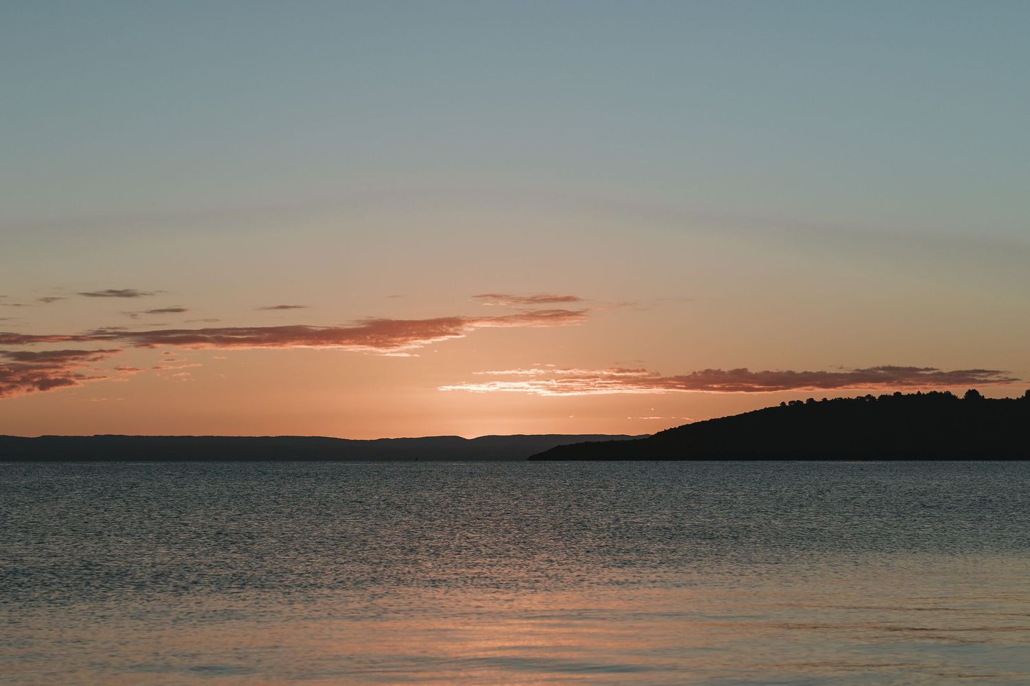 A serene sunset over tranquil ocean waters creates a mesmerizing orange and pink gradient in the sky and water.