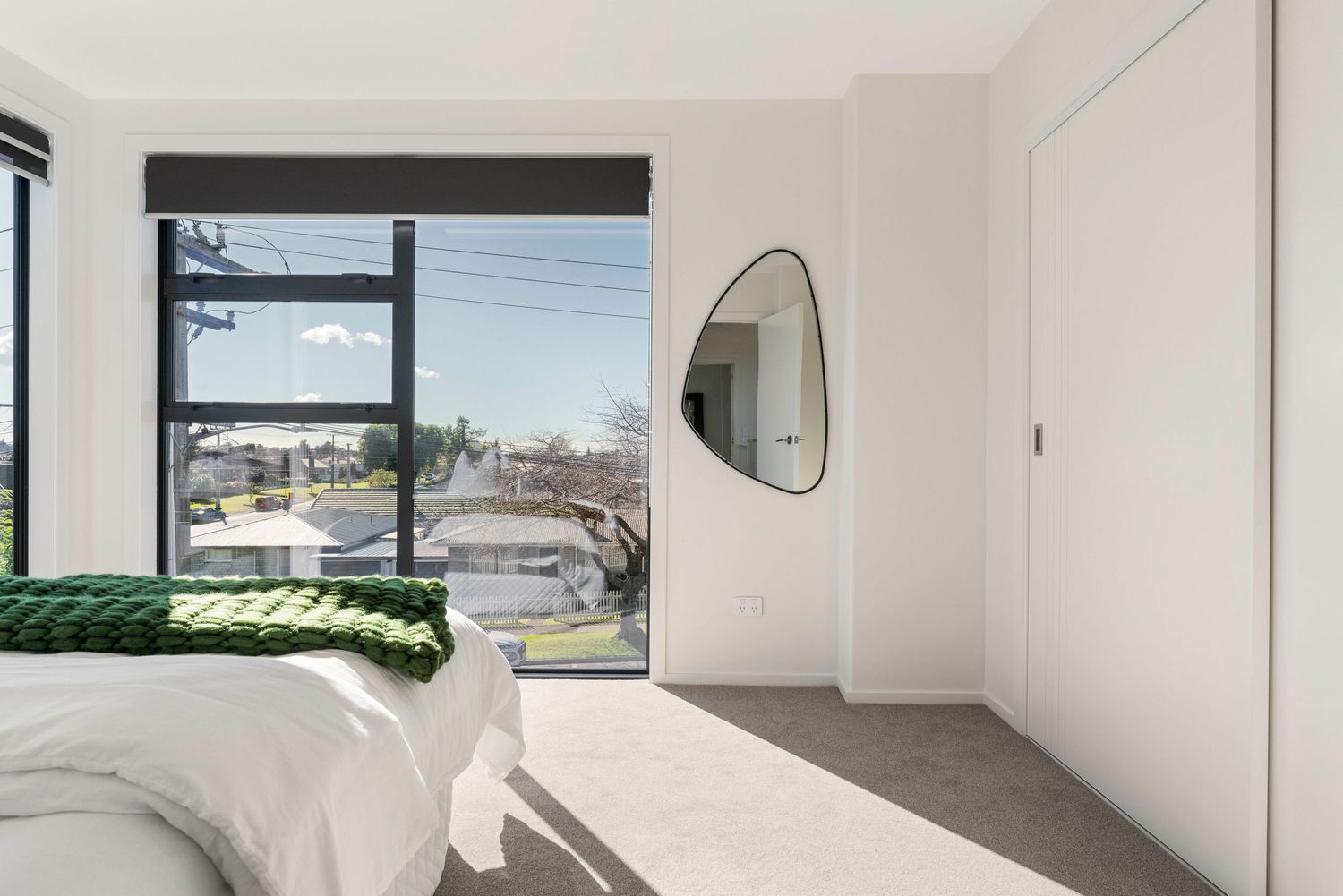 Sleek white bedroom with minimal decor features expansive windows and treetop views.