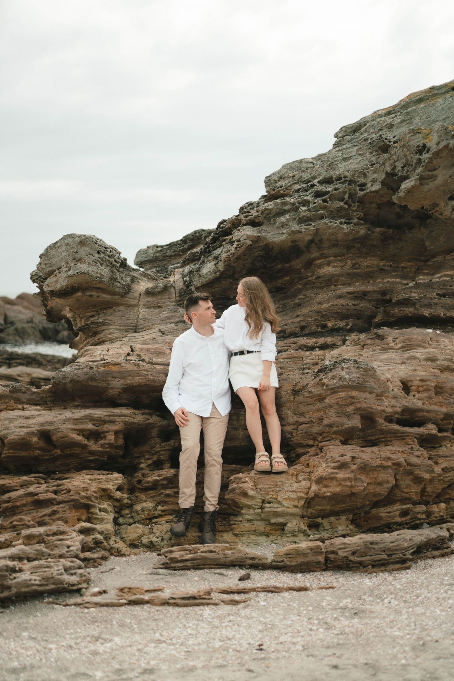 Two people in matching white outfits sitting on coastal rock formations.