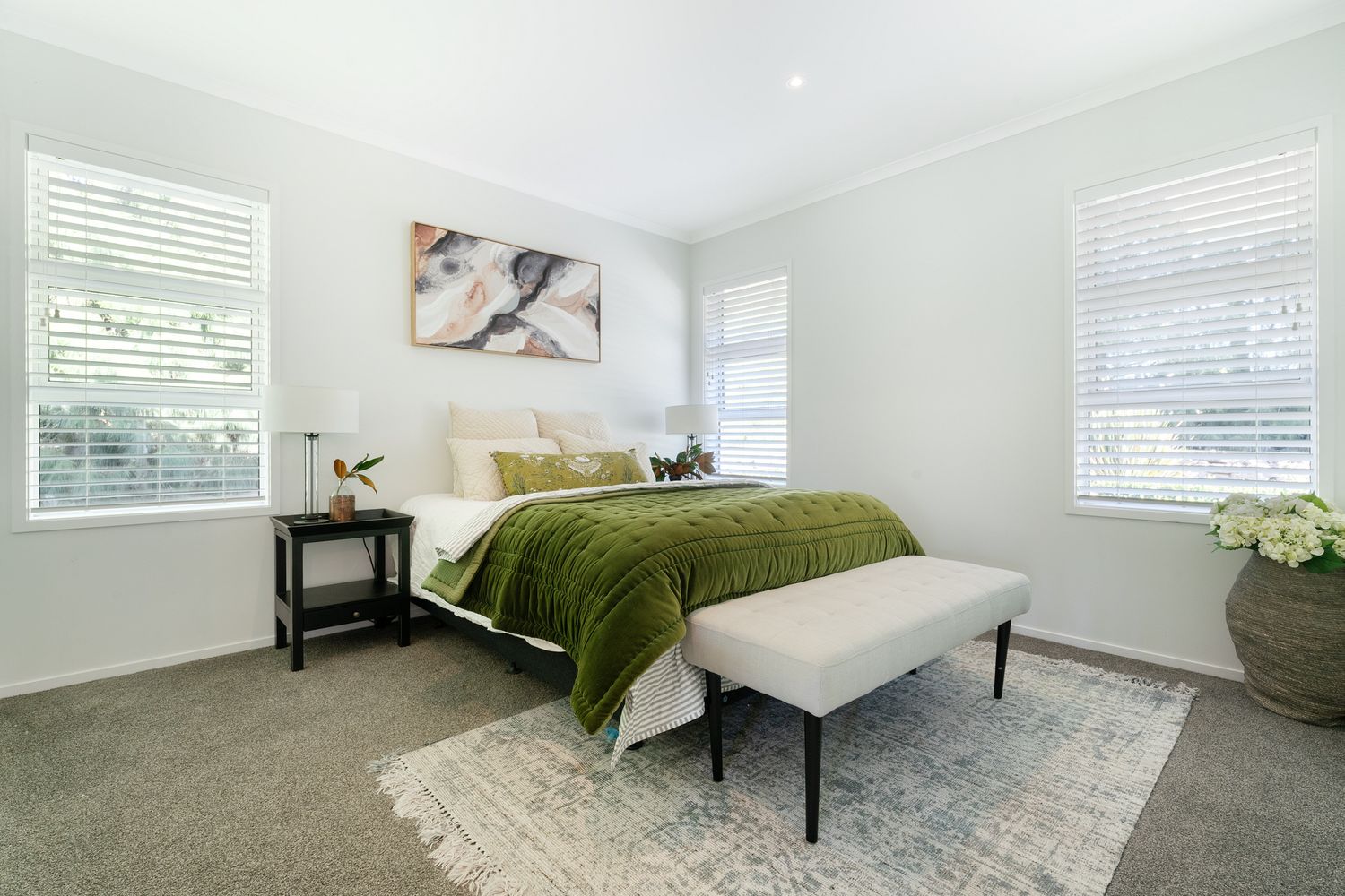 Modern bedroom with green bedspread, white walls, and natural light from venetian blinds.