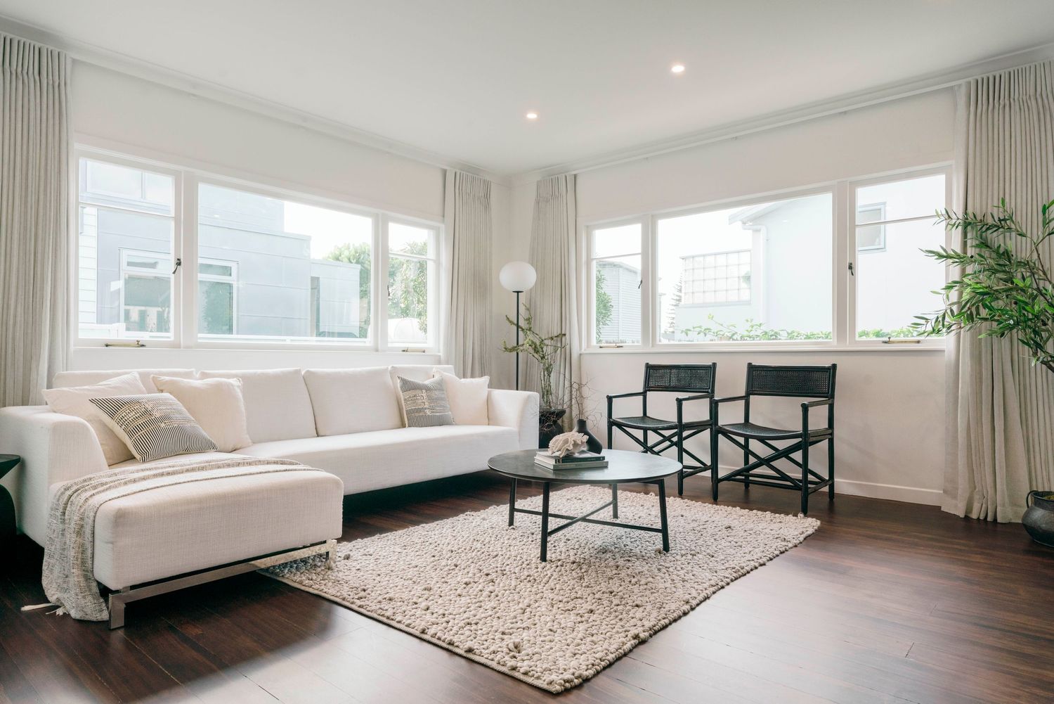Bright living room with white walls, large windows, and beige furniture on a plush carpet.