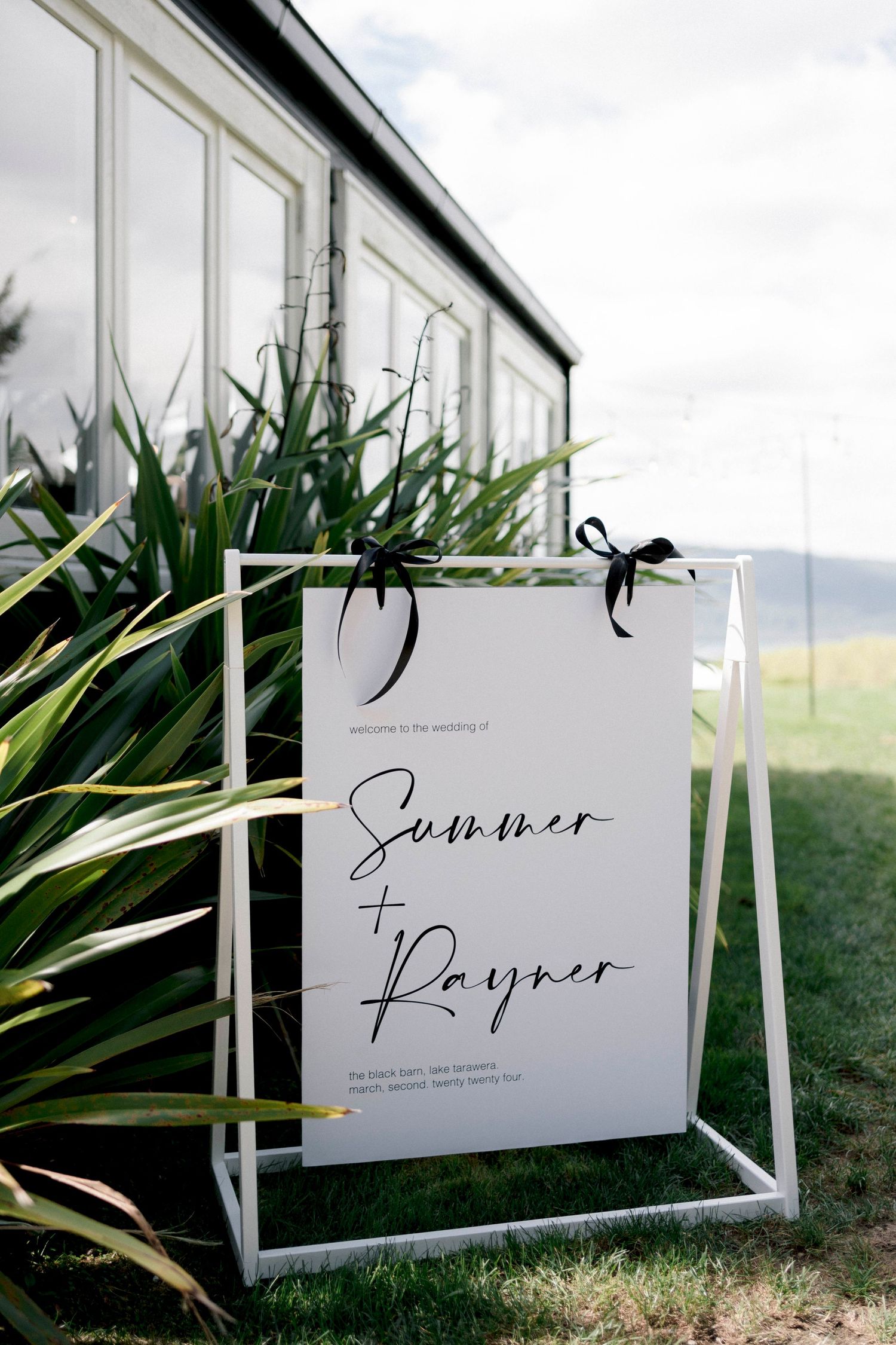 Elegant wedding sign with couple's names displayed in a modern white frame against lush greenery.