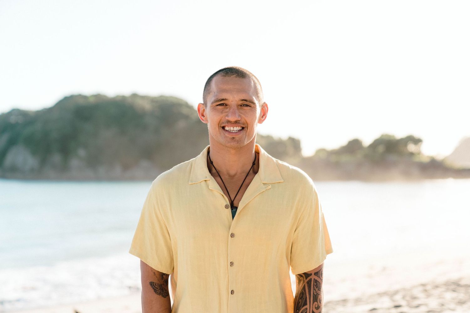 Man wearing yellow shirt smiles while standing on beach at sunset.