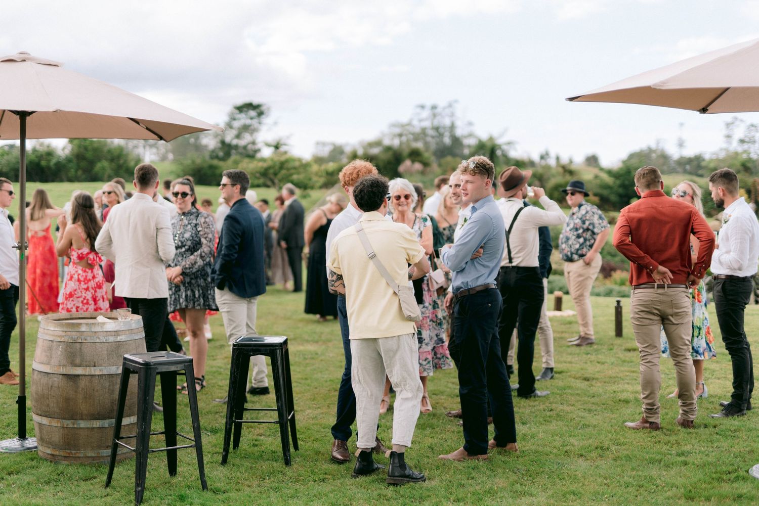 Guests mingle at an outdoor wedding reception with wine barrels and patio umbrellas.
