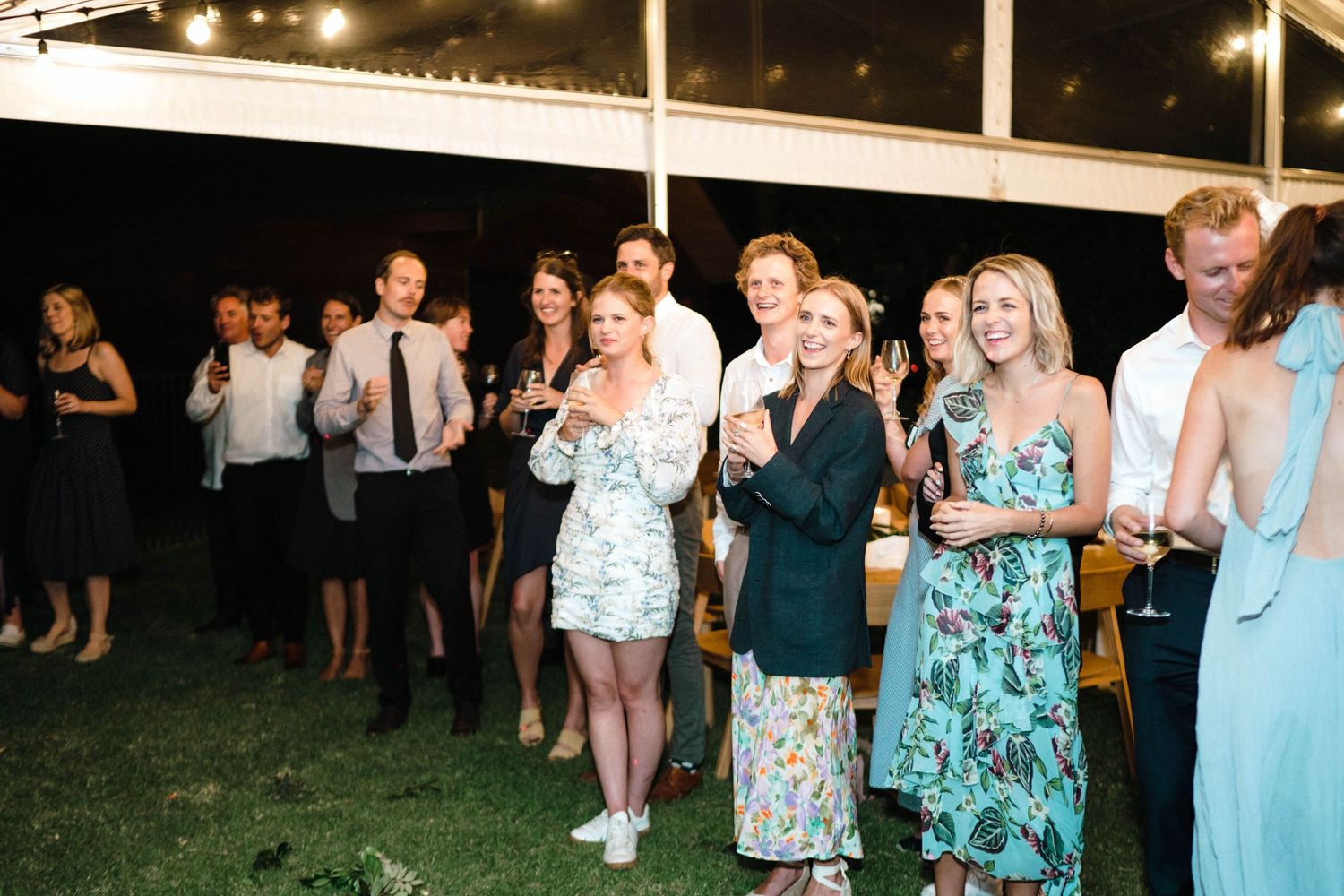 Wedding guests dancing in groups under string lights at an outdoor reception.